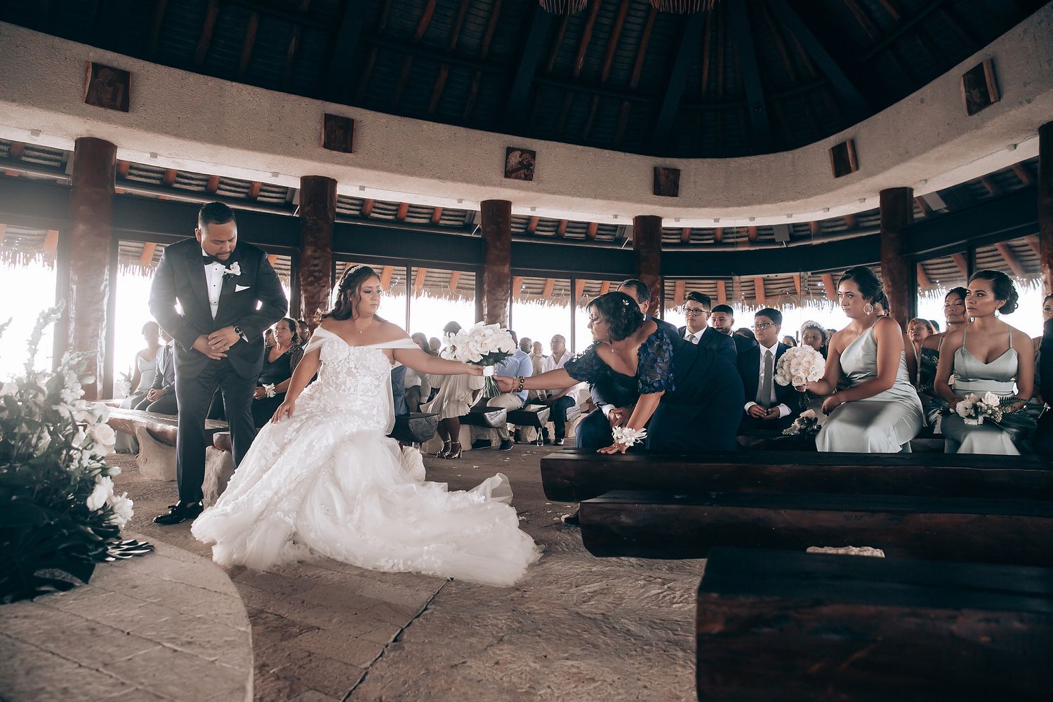 Wedding ceremony taking place in a rustic circular pavilion with wooden benches and natural lighting.