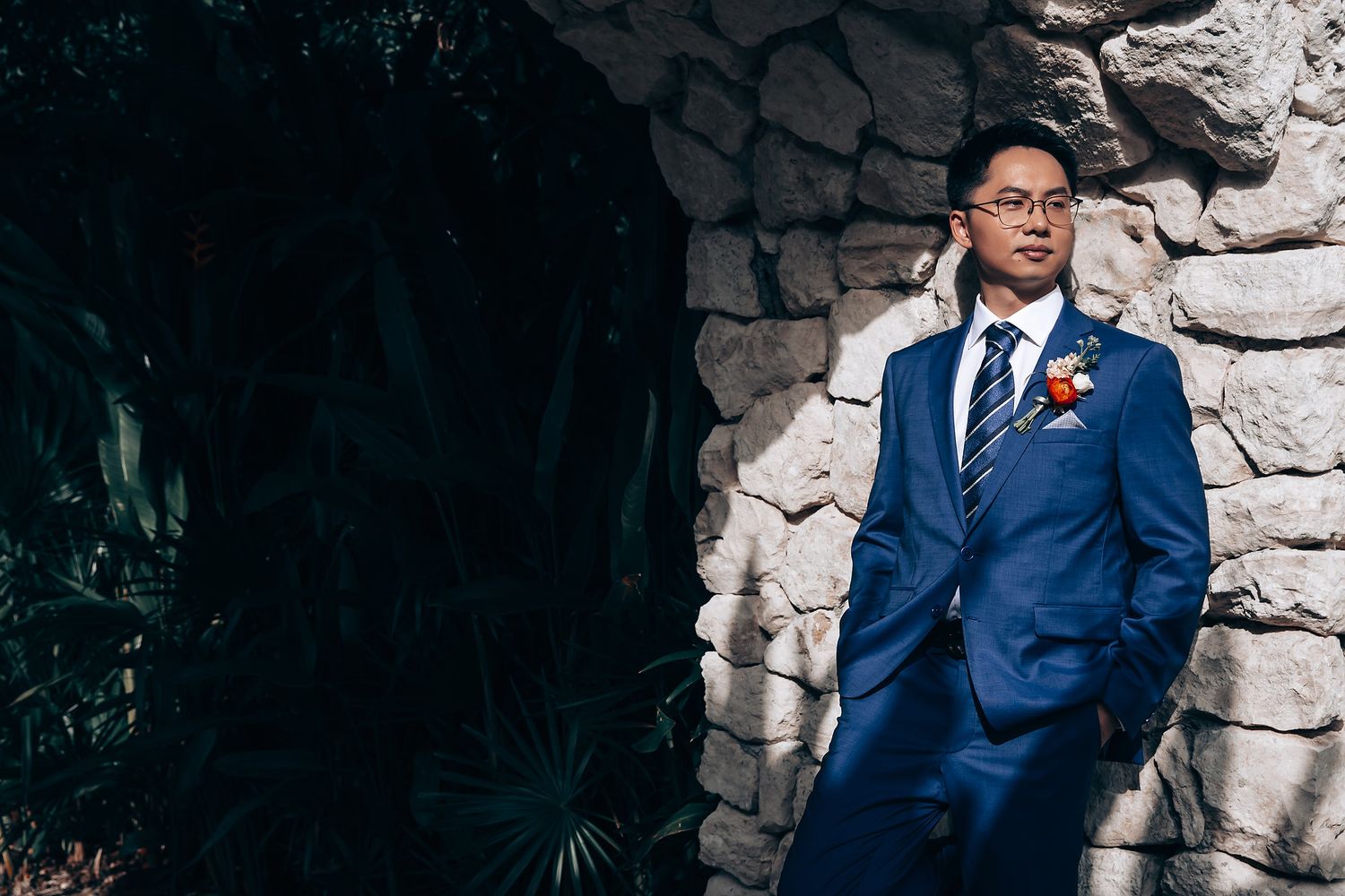 A series of six professional portraits against a stone wall showing someone in a navy blue suit and red tie.