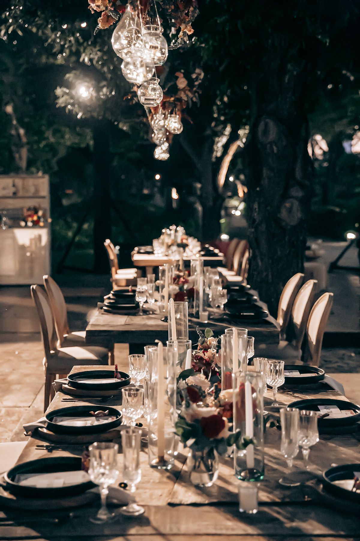Elegant wedding reception table setting with black plates, crystal glassware, and hanging lights creating a moody atmosphere.