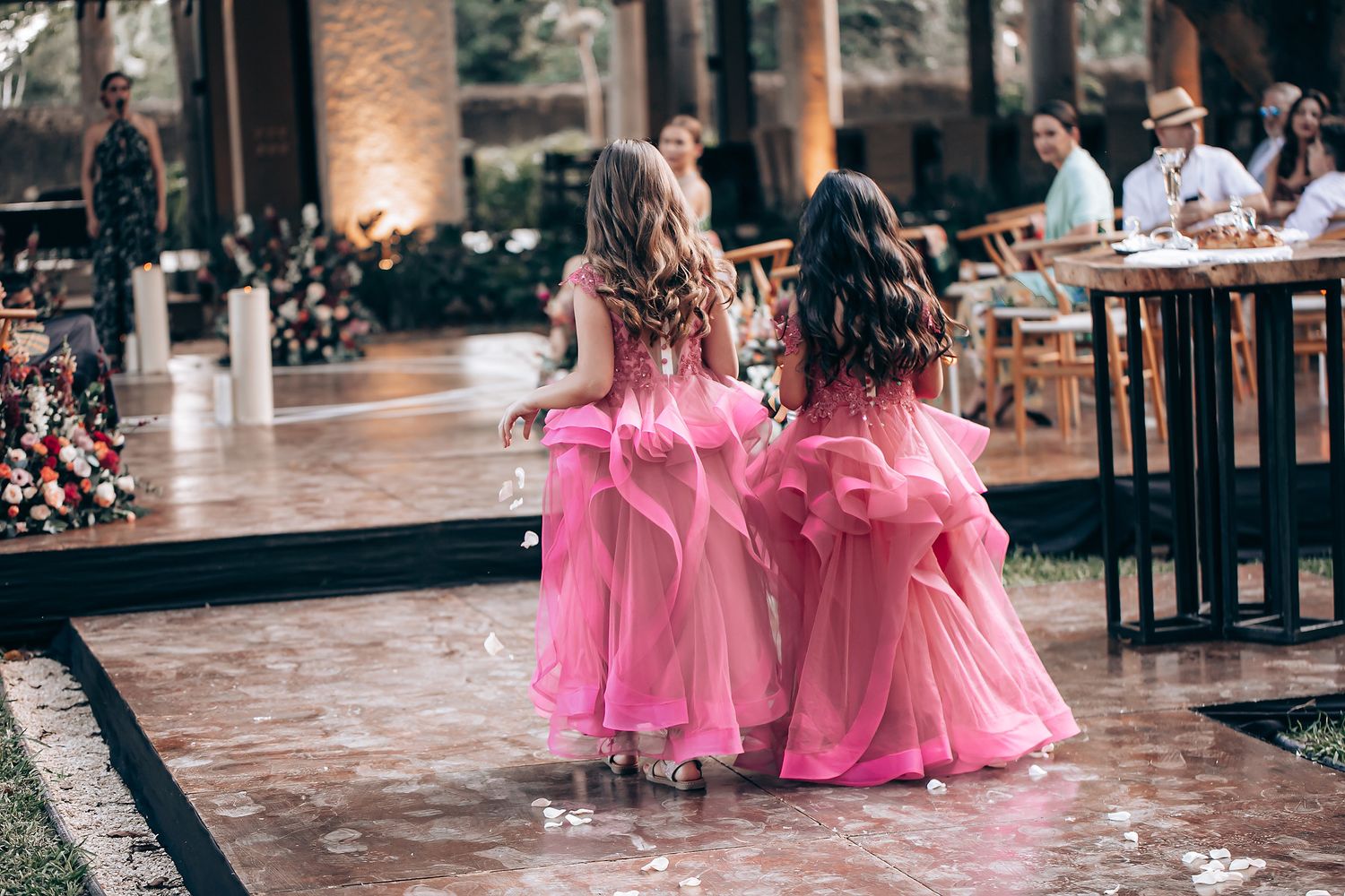 Two young attendants in matching pink dresses walk together on a polished floor at an indoor event space.