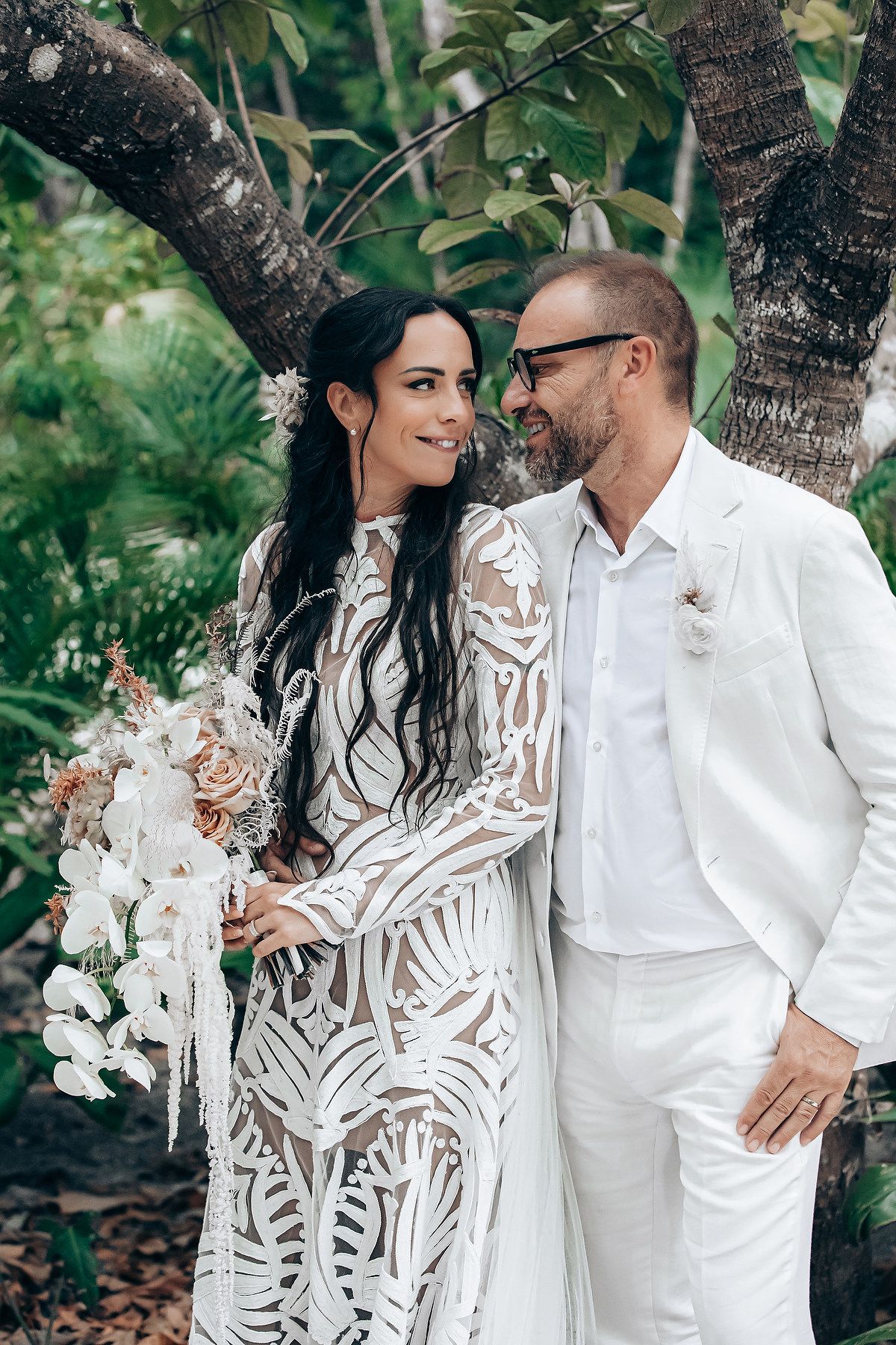 A couple in elegant white attire shares romantic moments in a garden setting.