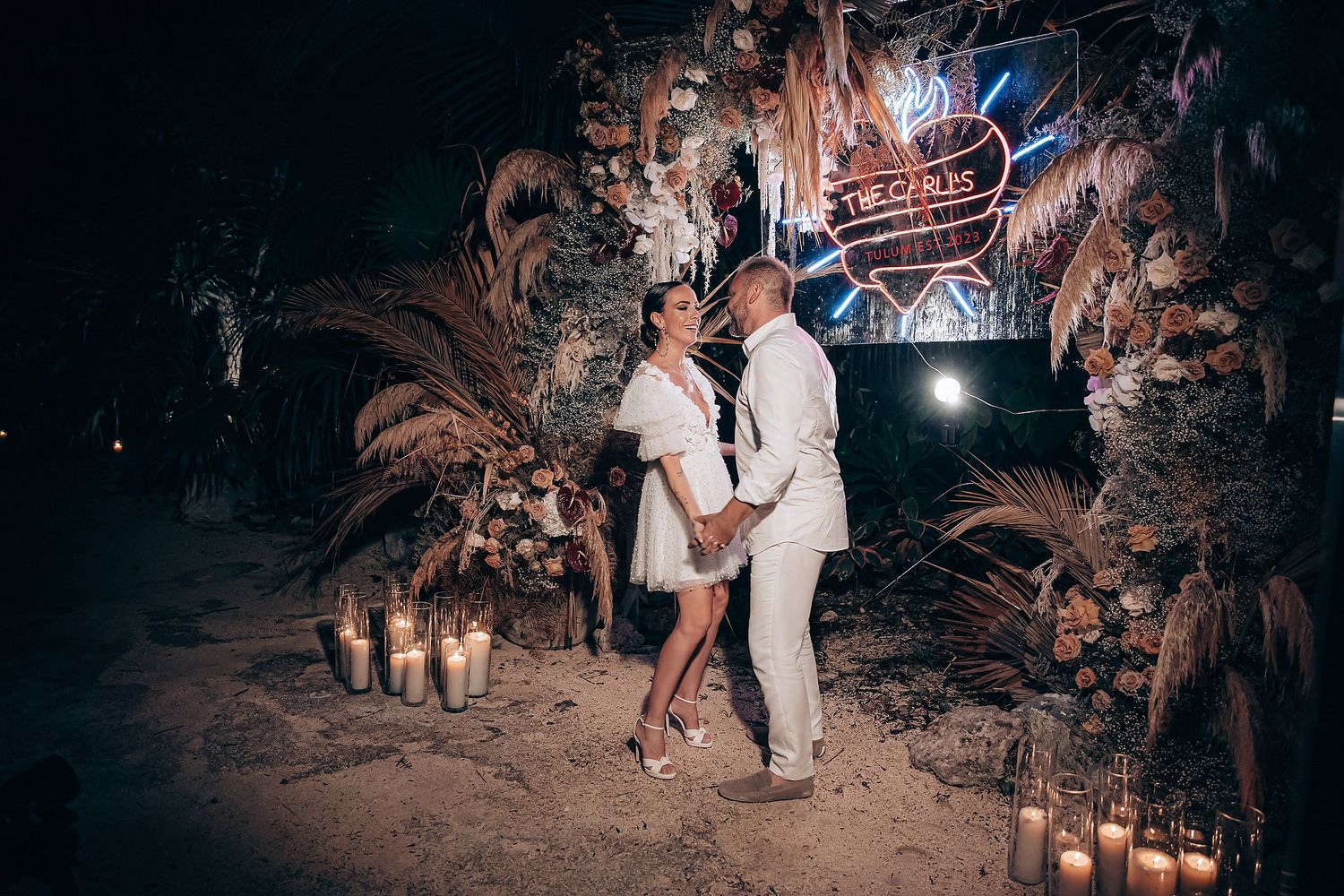 Guests dancing and celebrating at a nighttime outdoor wedding reception under string lights and palm trees.