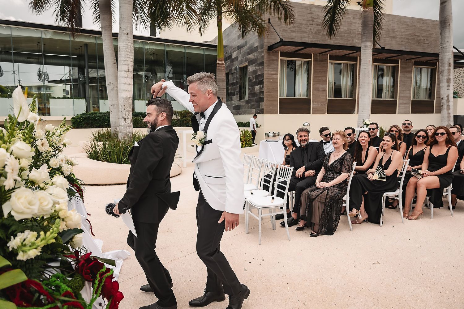 Wedding ceremony setup with palm trees and guests seated in rows outdoors.