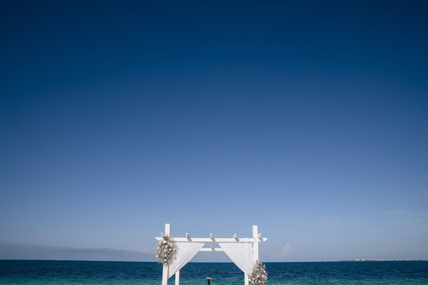 Panoramic sequence of a white wedding arch setup on a beach with blue ocean and sky in the background.