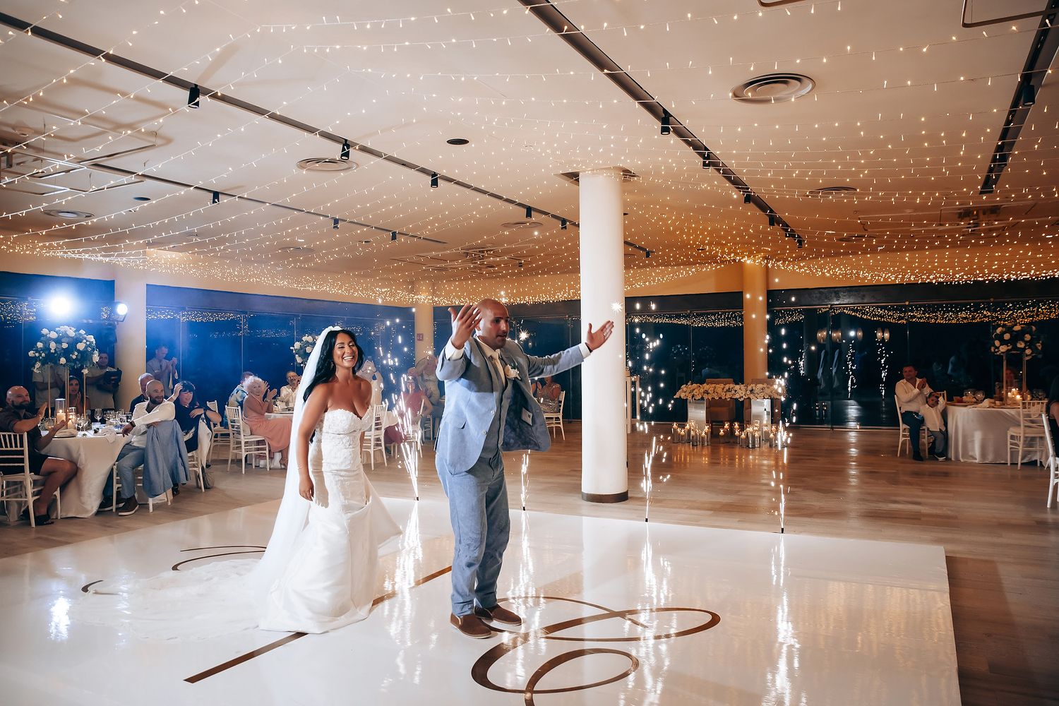 A large indoor roller skating rink with string lights hanging from the ceiling and people skating on the wooden floor.