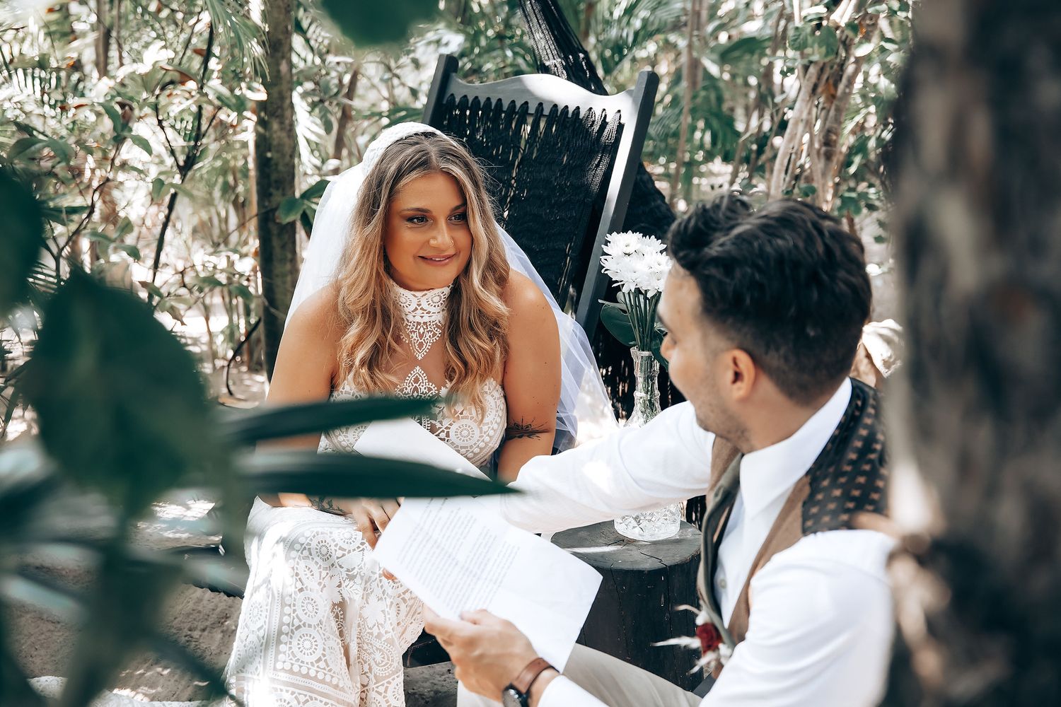 Couple in white wedding attire exchange vows during an outdoor garden ceremony.