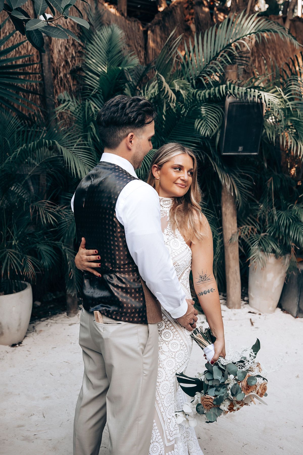 A bride and groom share intimate moments in a tropical garden setting with palm trees in the background.