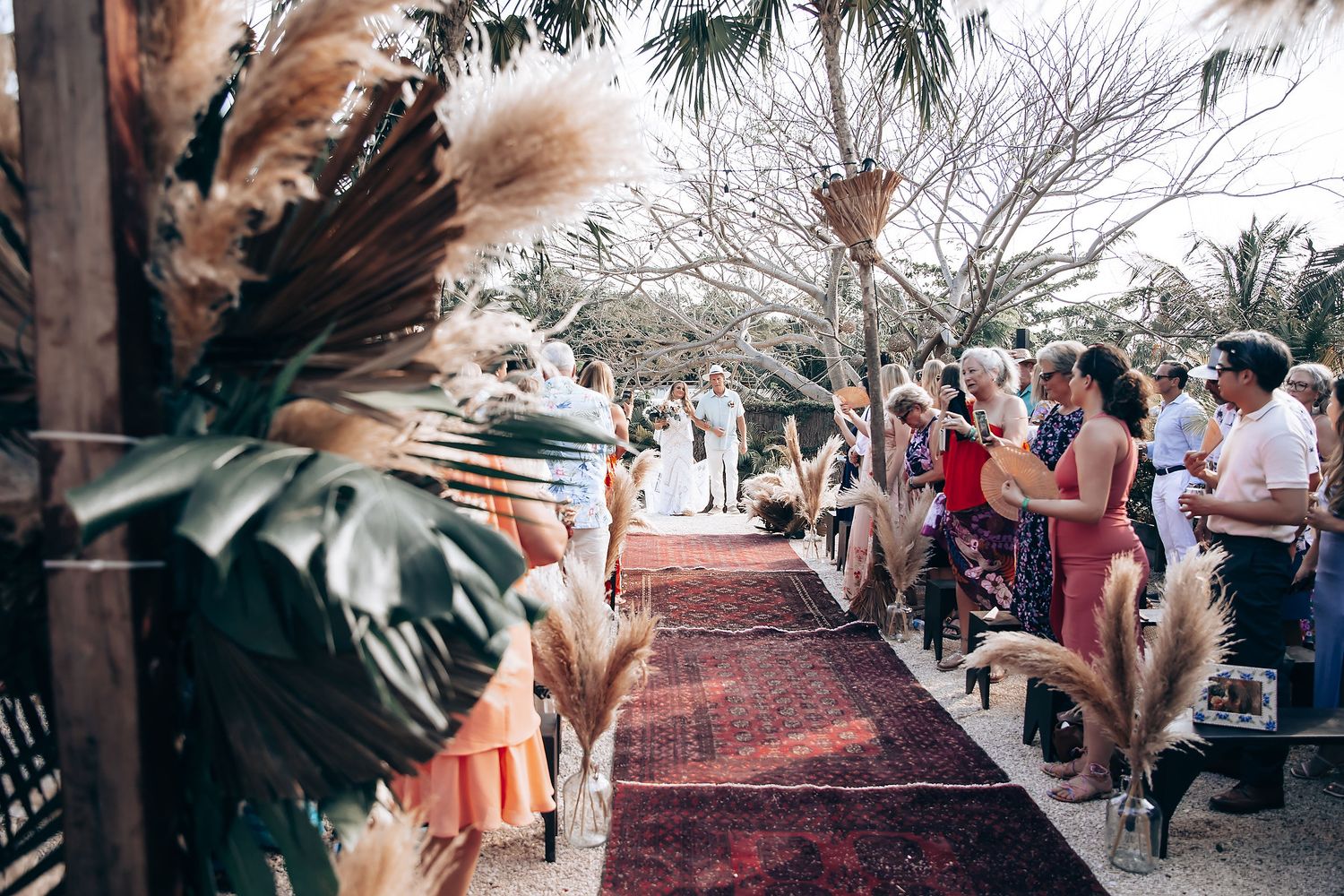 Wedding guests mingle under string lights and palm trees at a tropical outdoor reception.