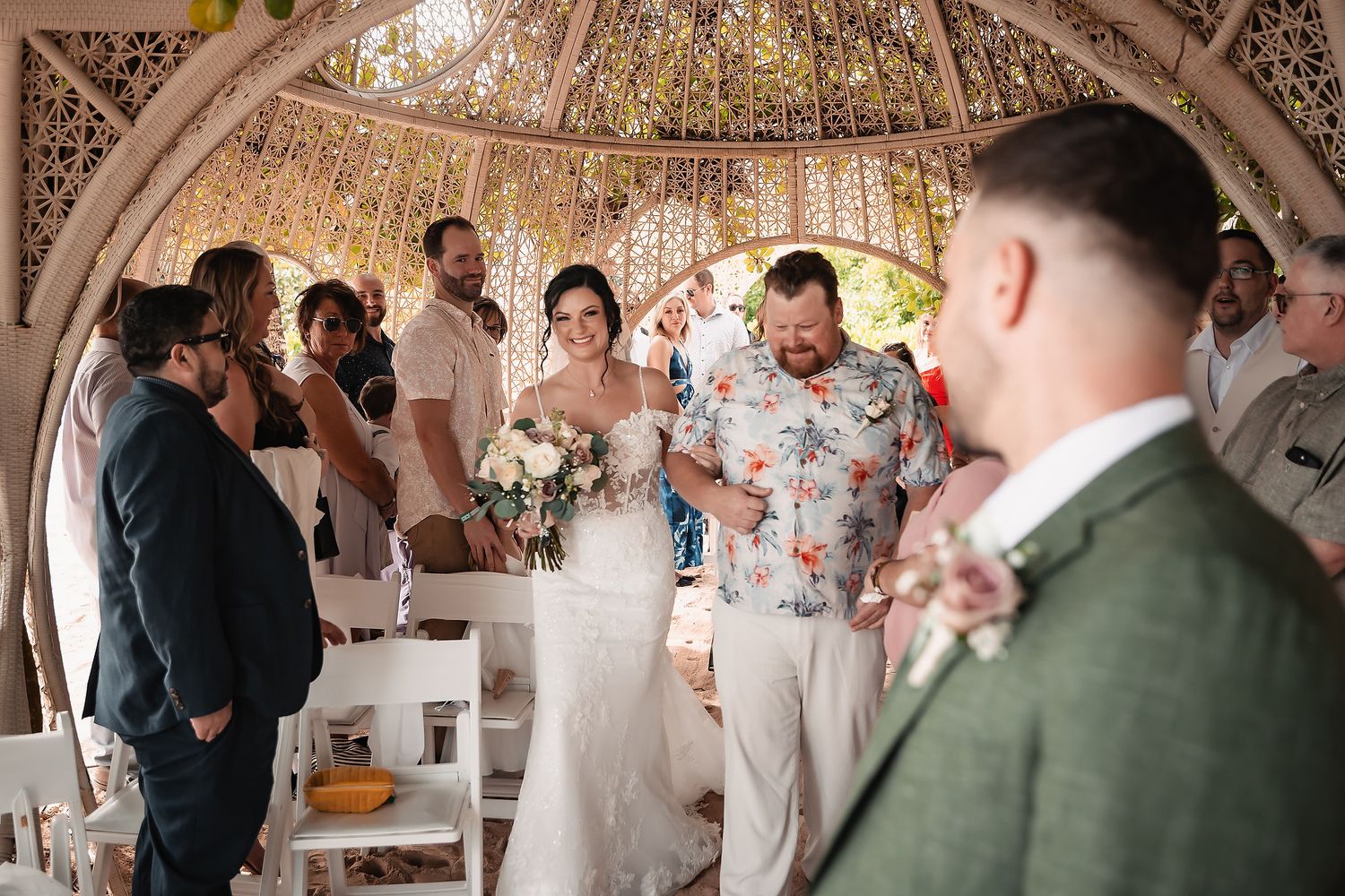 Wedding ceremony guests gathered under an ornate gazebo with intricate lattice details.