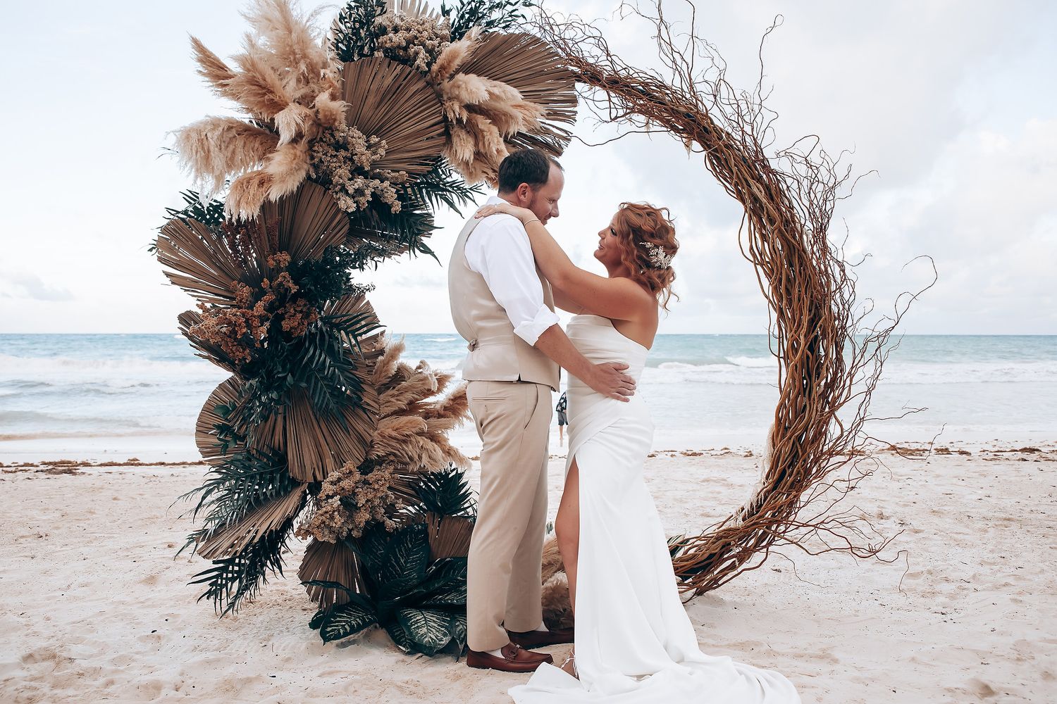 Elegant beach ceremony setup with dried palm leaves and pampas grass arrangements.