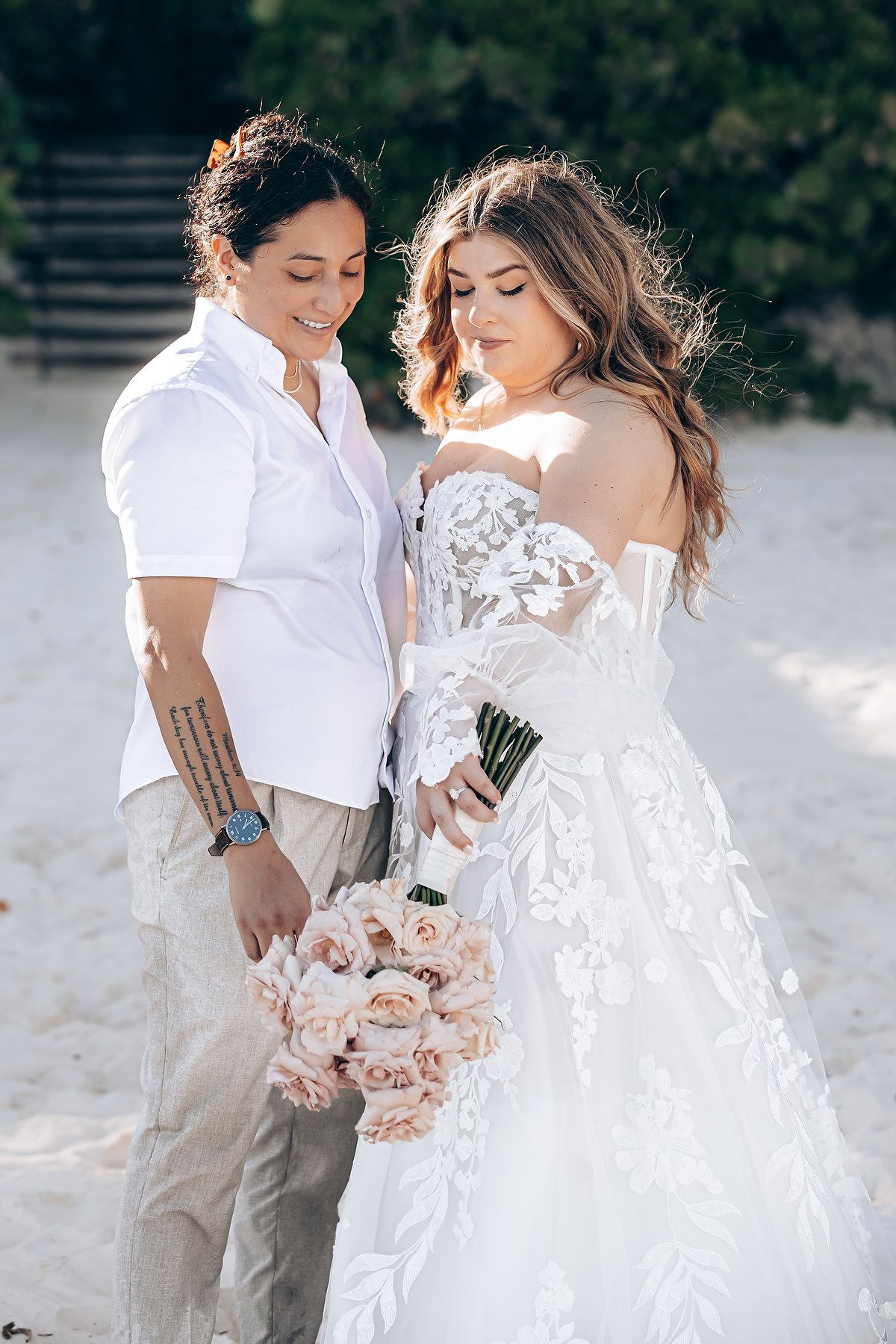 A romantic beach wedding portrait featuring a couple in white attire with pink roses.