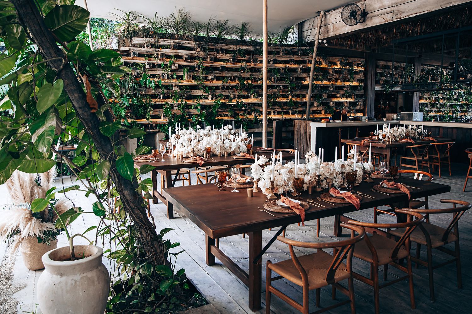Lush greenery surrounds a contemporary dining area with wooden tables and white decor.