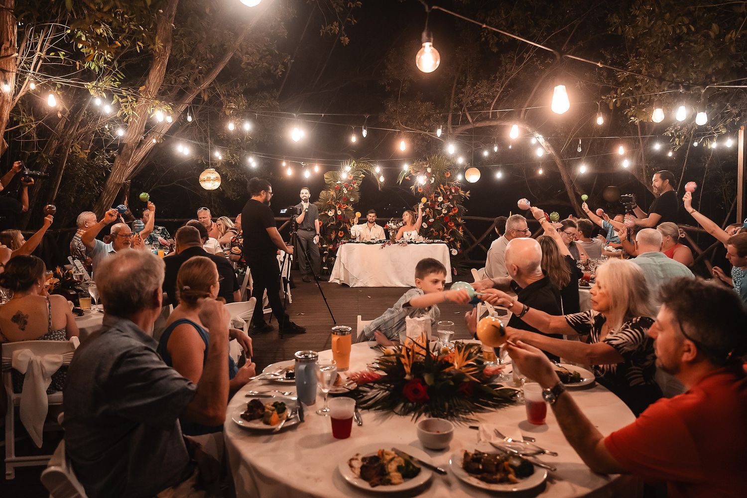 Wedding guests enjoying dinner under warm string lights at outdoor reception.