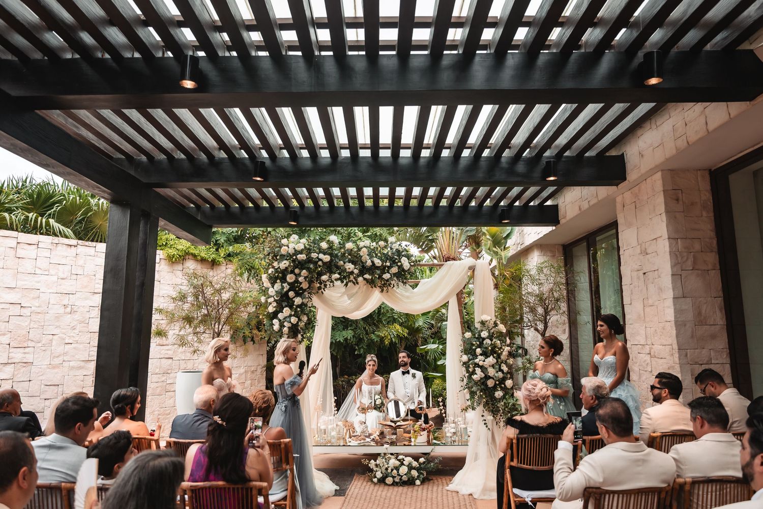 Wedding ceremony setup under a modern pergola with floral arch and white draping.