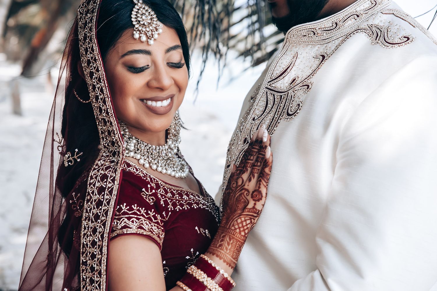 Close-up of intricate bridal jewelry and burgundy wedding attire details.