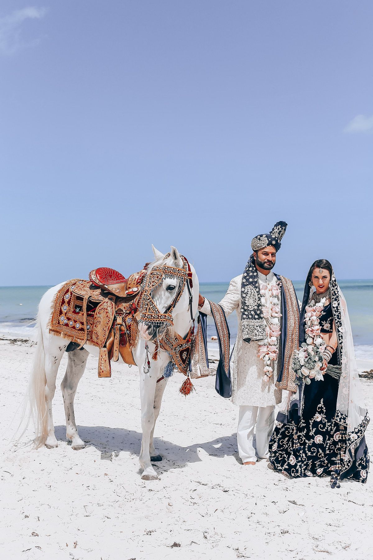 White horses adorned with wedding decorations line up on a pristine beach.