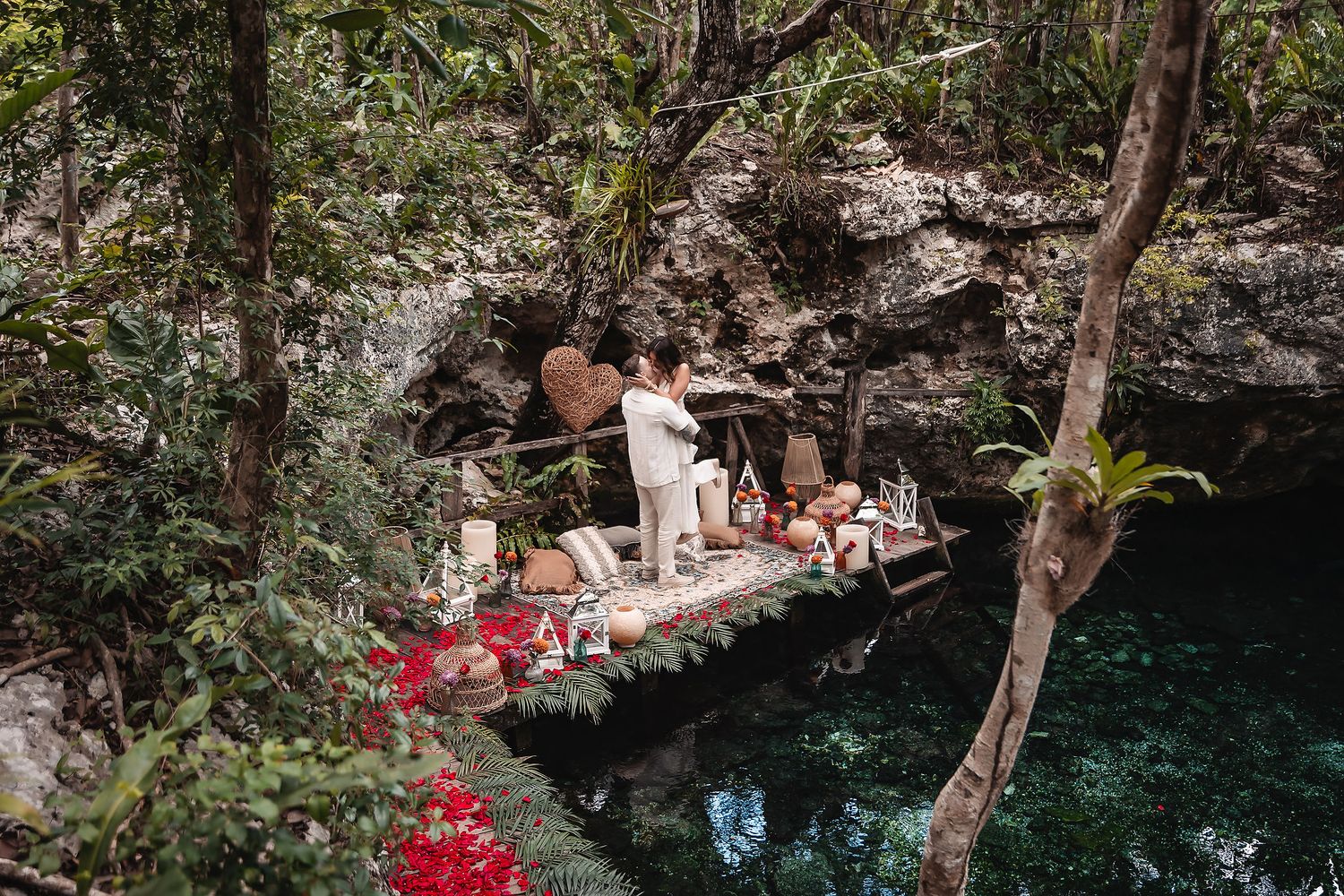 Decorated wooden platform over crystal clear cenote waters with red flowers.