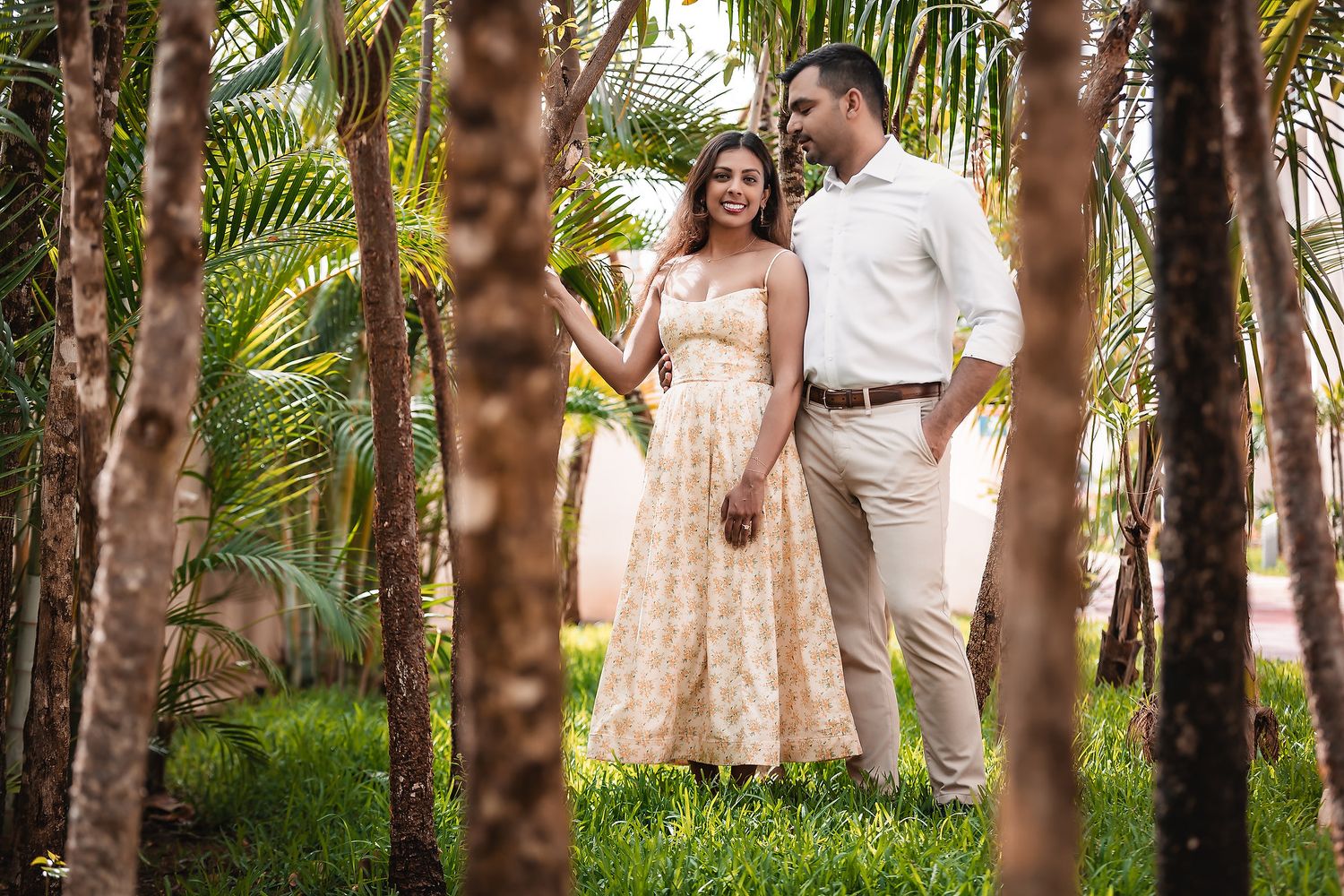 Couple shares intimate moments among palm trees in a lush garden setting.