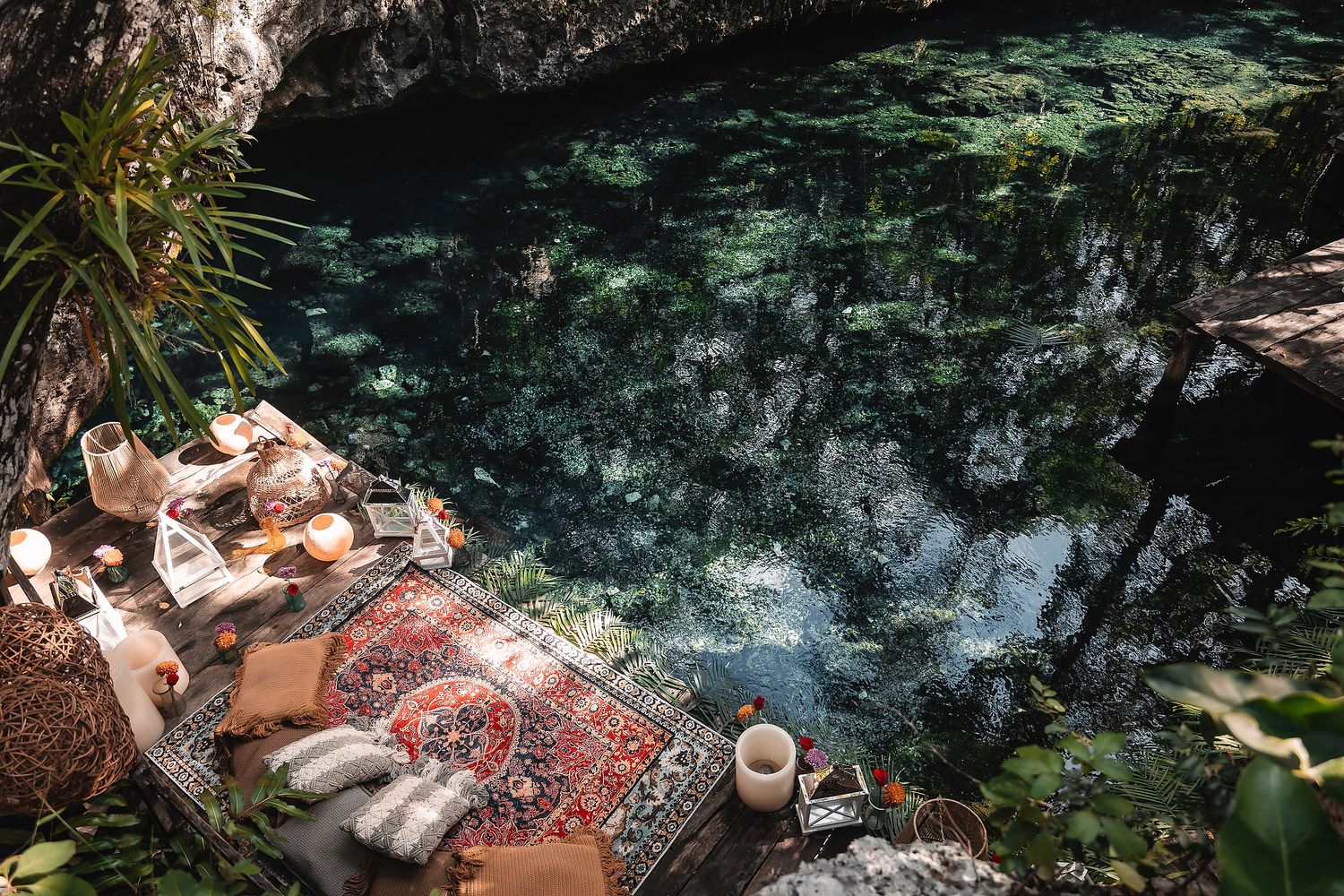 Cozy picnic setup with rugs and pillows along a turquoise cenote in Mexico.