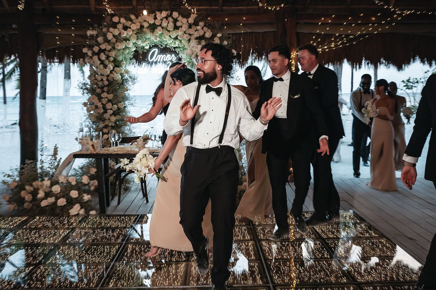 Groom dances with bride during fun wedding reception entrance on a mirrored dance floor beneath a floral arch.
