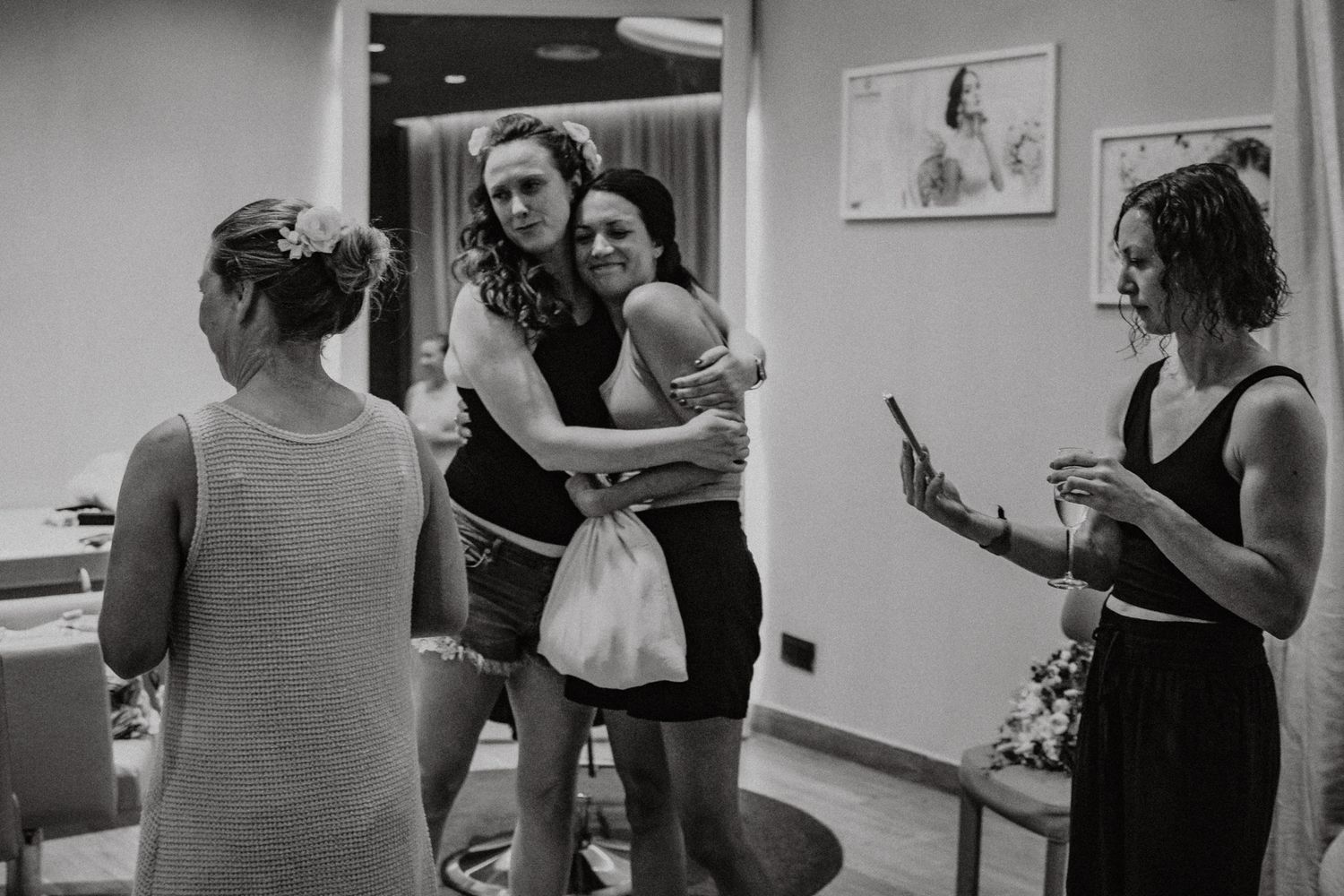 Black and white photo of women hugging and sharing joyful moments during a wedding preparation gathering.