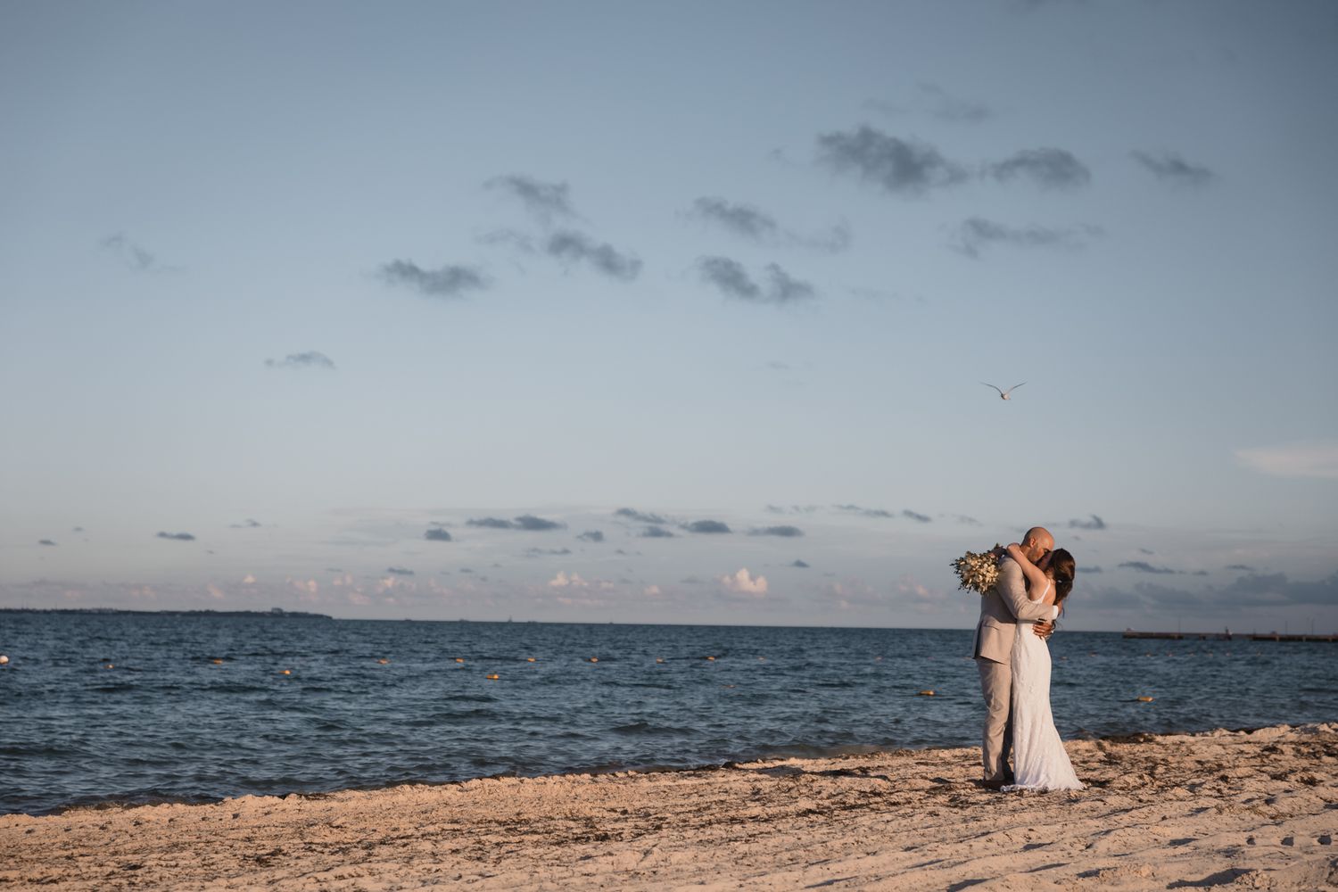 Couple embracing on a sandy beach at sunset during their wedding ceremony by the ocean.