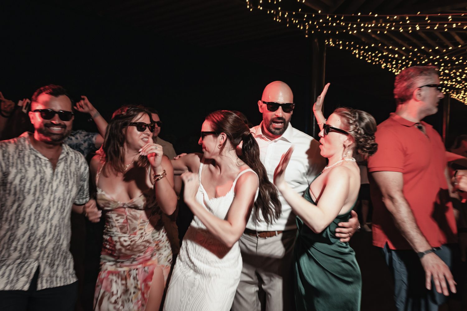 Guests dancing and celebrating at an outdoor wedding reception under string lights at night.