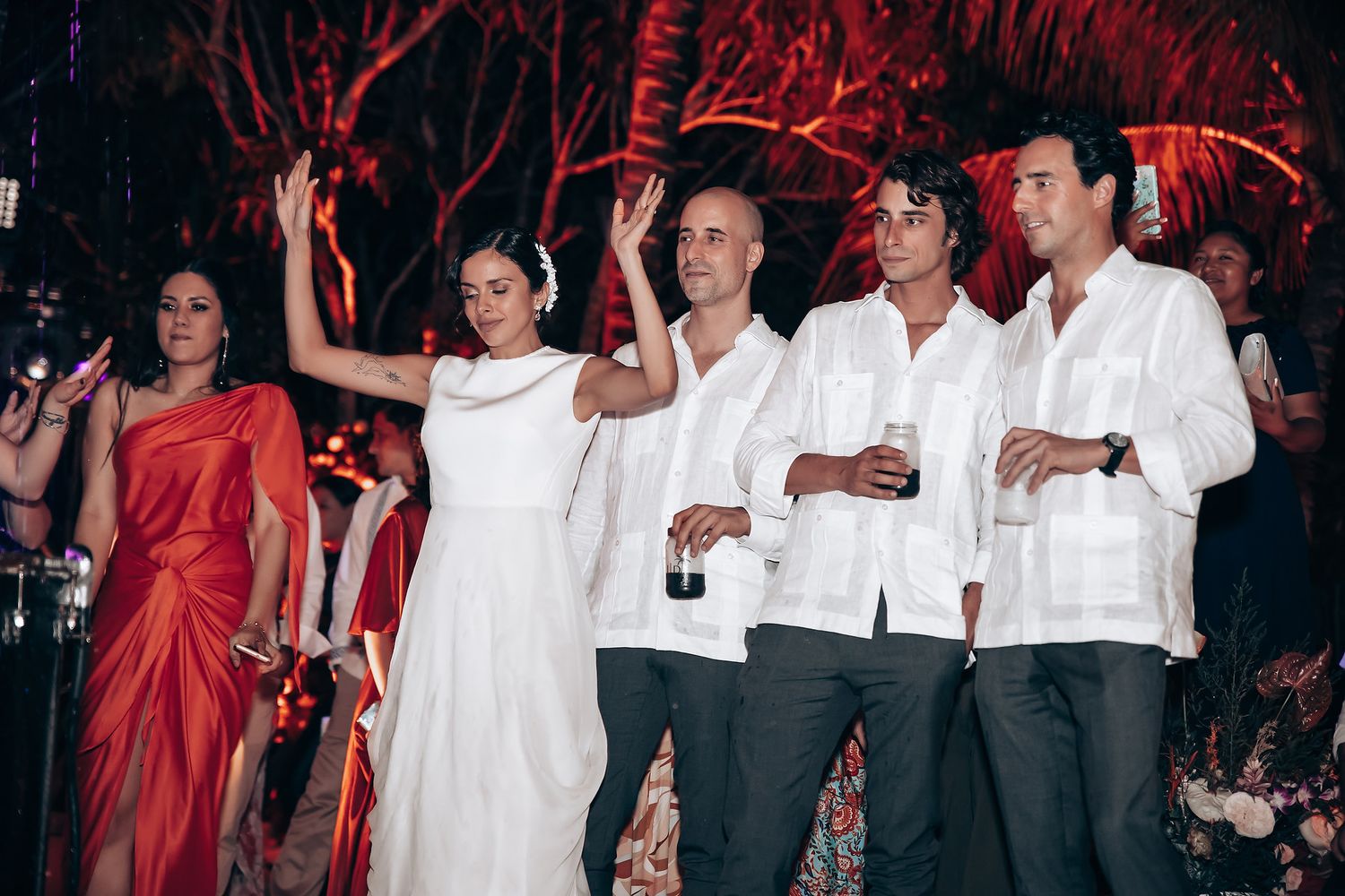 Group of party guests in white formal attire celebrating at an outdoor evening event.