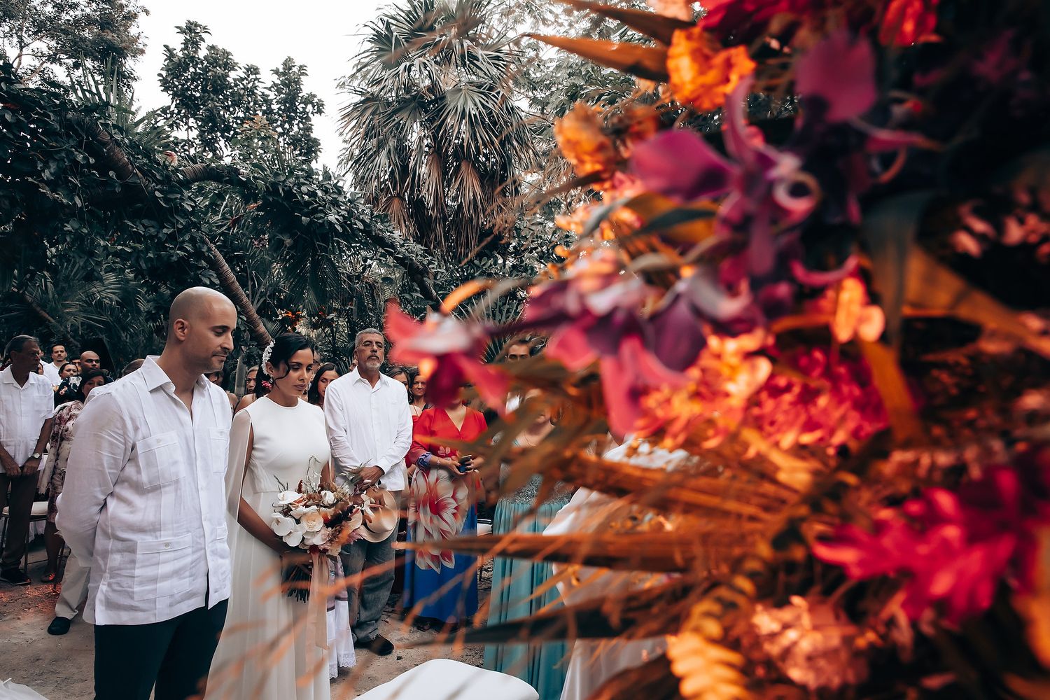 Wedding ceremony in lush tropical garden setting with vibrant red flowers.