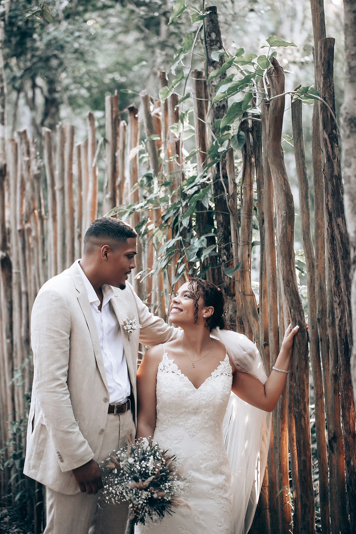 A romantic wedding couple shares intimate moments in a wooded setting with rustic wooden fences.