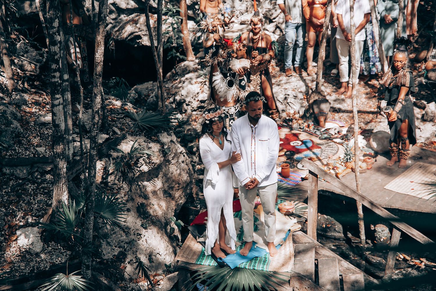 An outdoor celebration takes place on a wooden deck surrounded by natural forest scenery.
