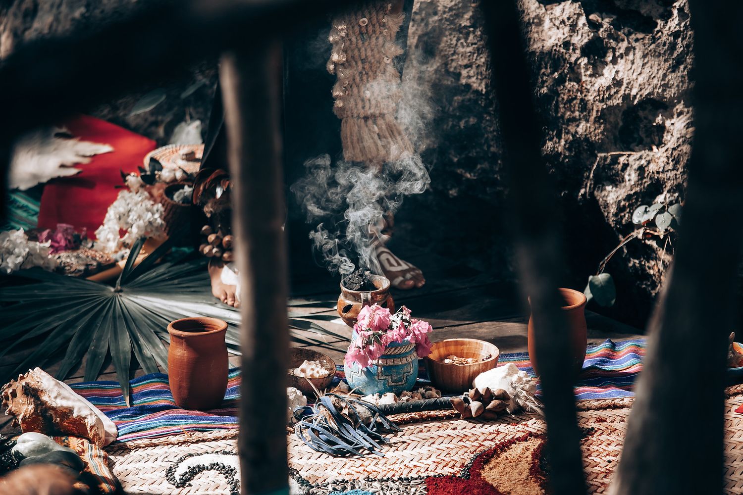 Colorful blankets and textiles laid out on the ground at an outdoor market display with sunlight filtering through trees.