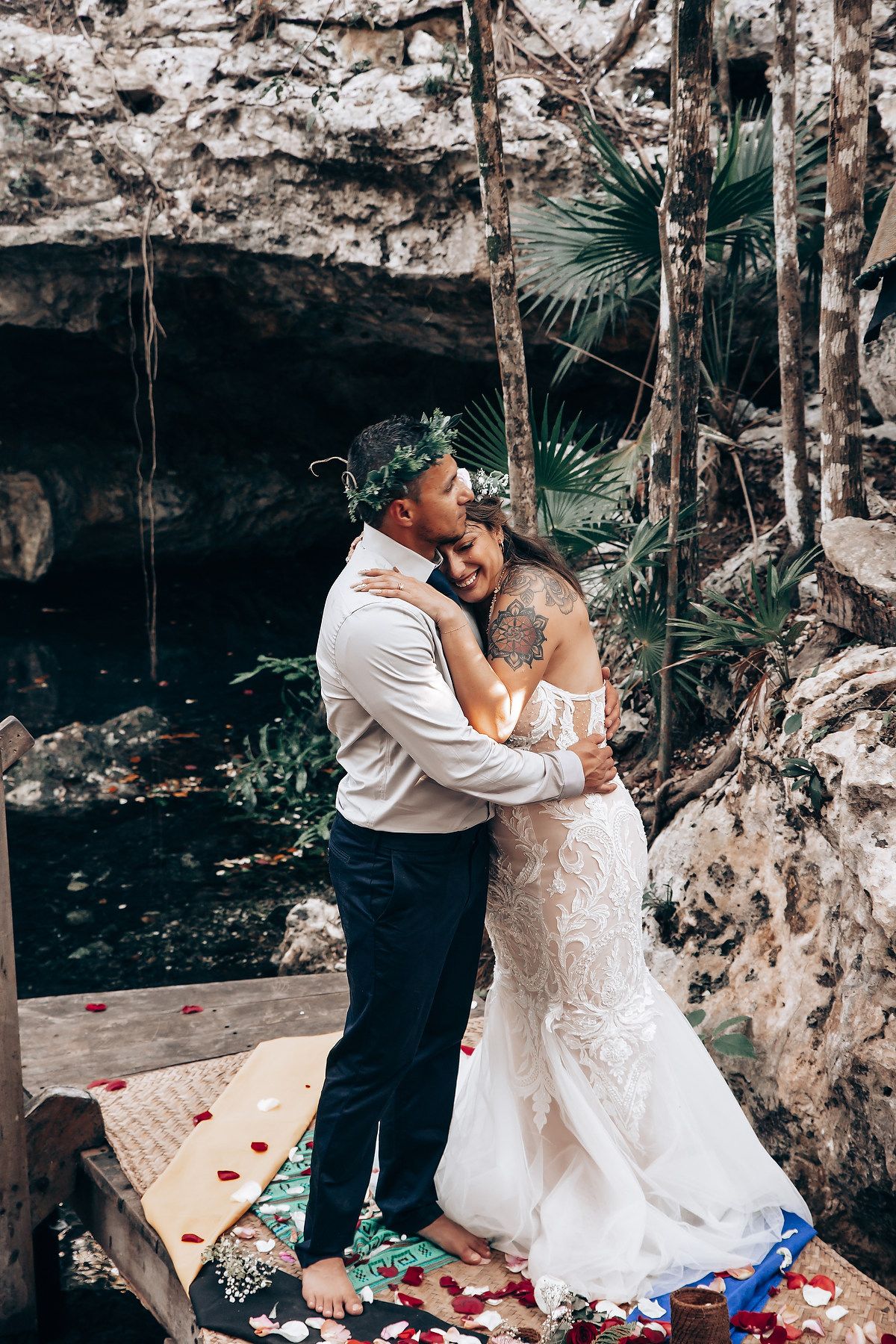A romantic moment unfolds on rose petals in a naturally lit cave during an intimate wedding ceremony.