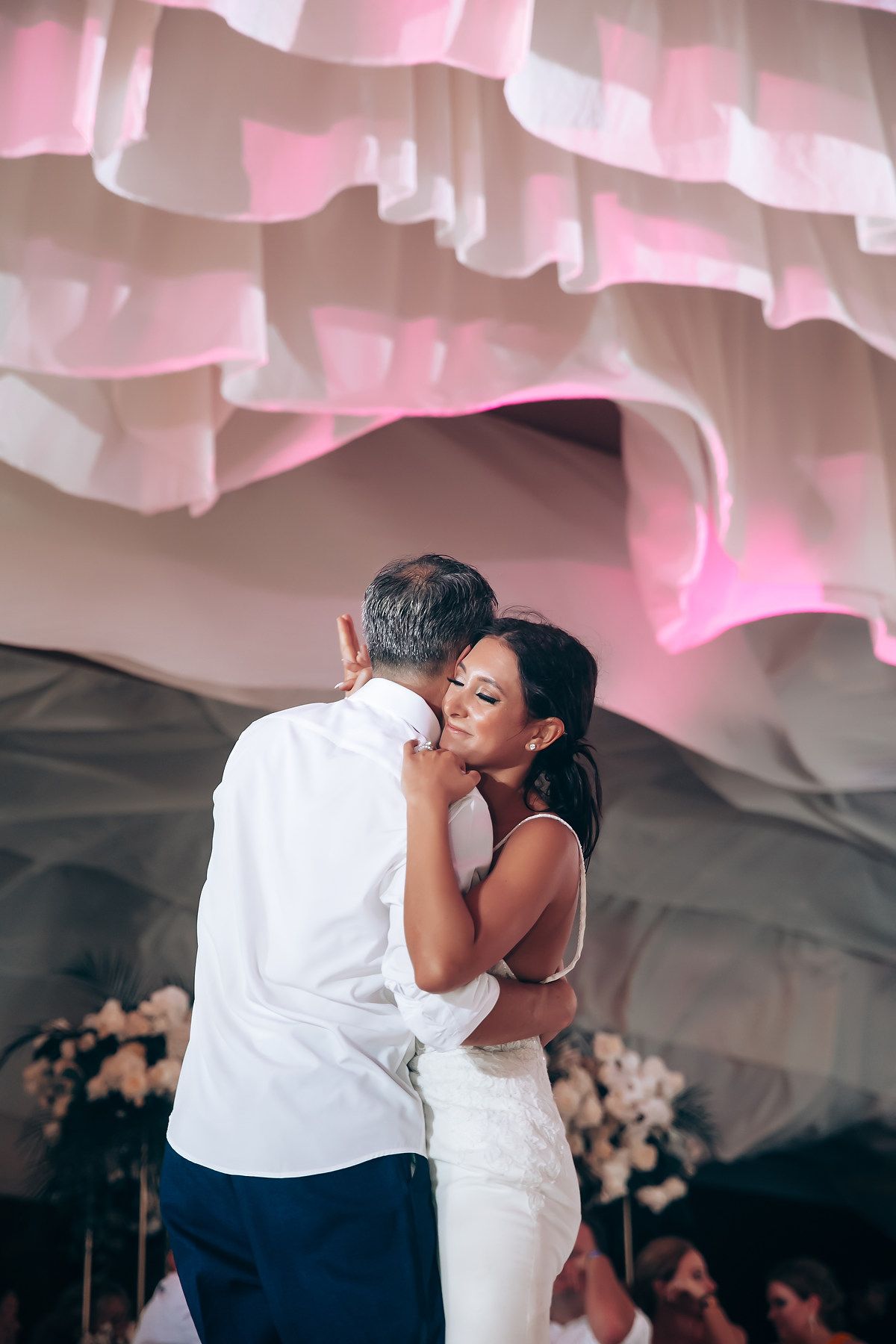 Romantic first dance moment under soft pink lighting and draped fabric ceiling decor.