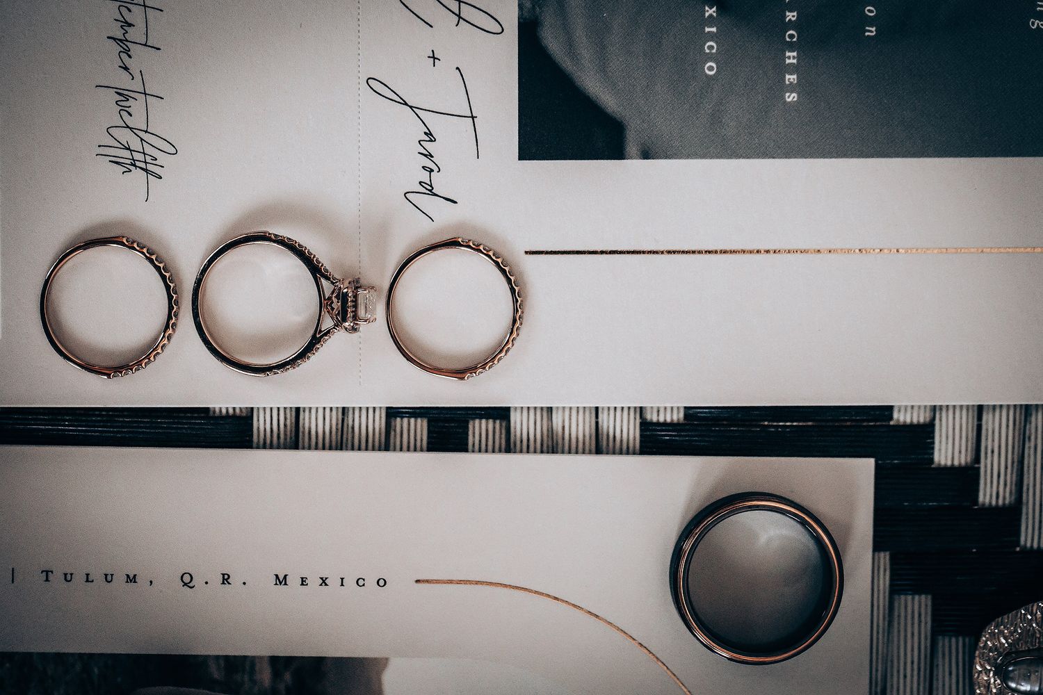 Wedding rings arranged artistically on paper documents with elegant calligraphy in a moody lighting setup.