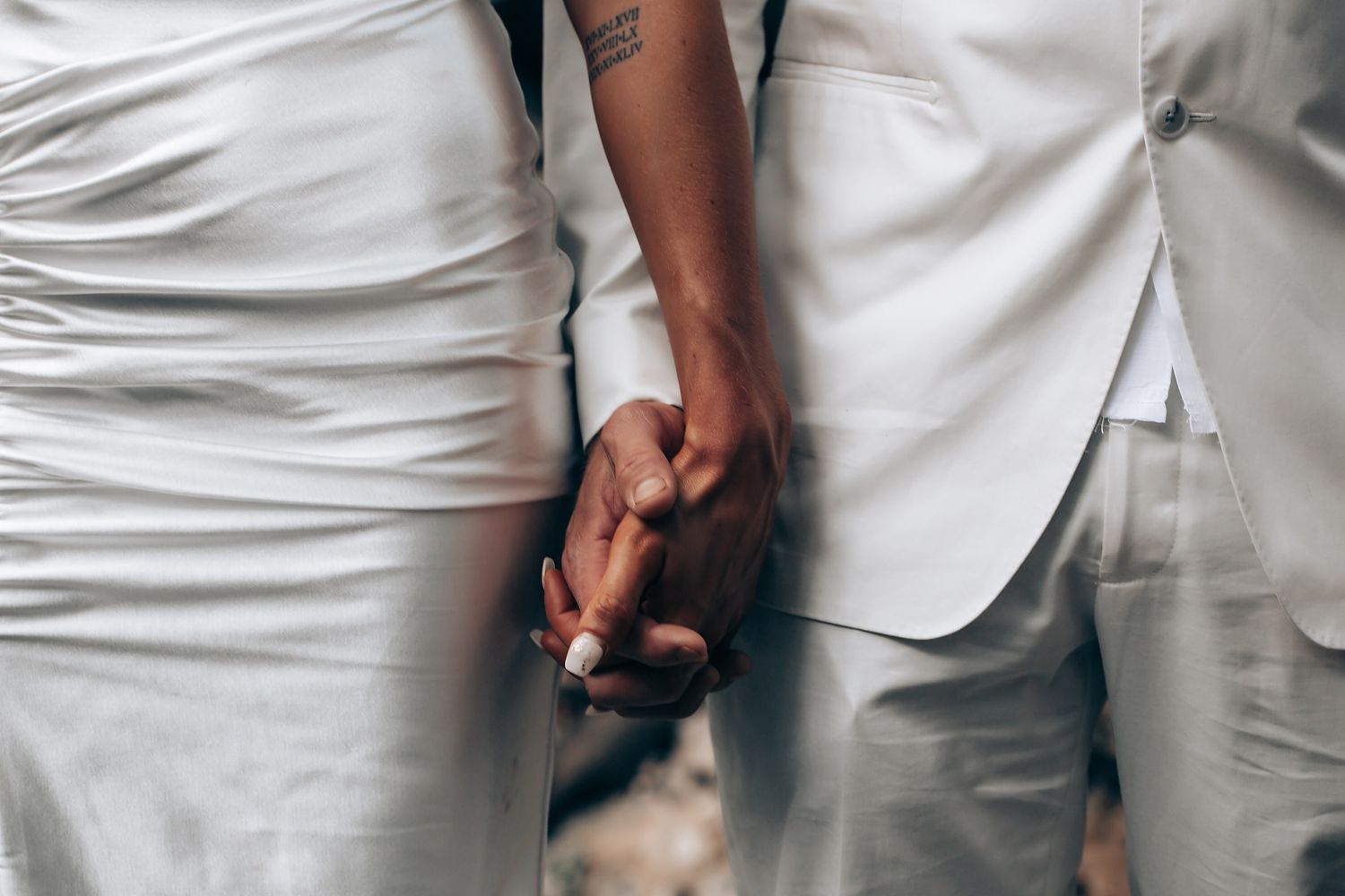 Close-up of hands clasped together wearing white formal attire.