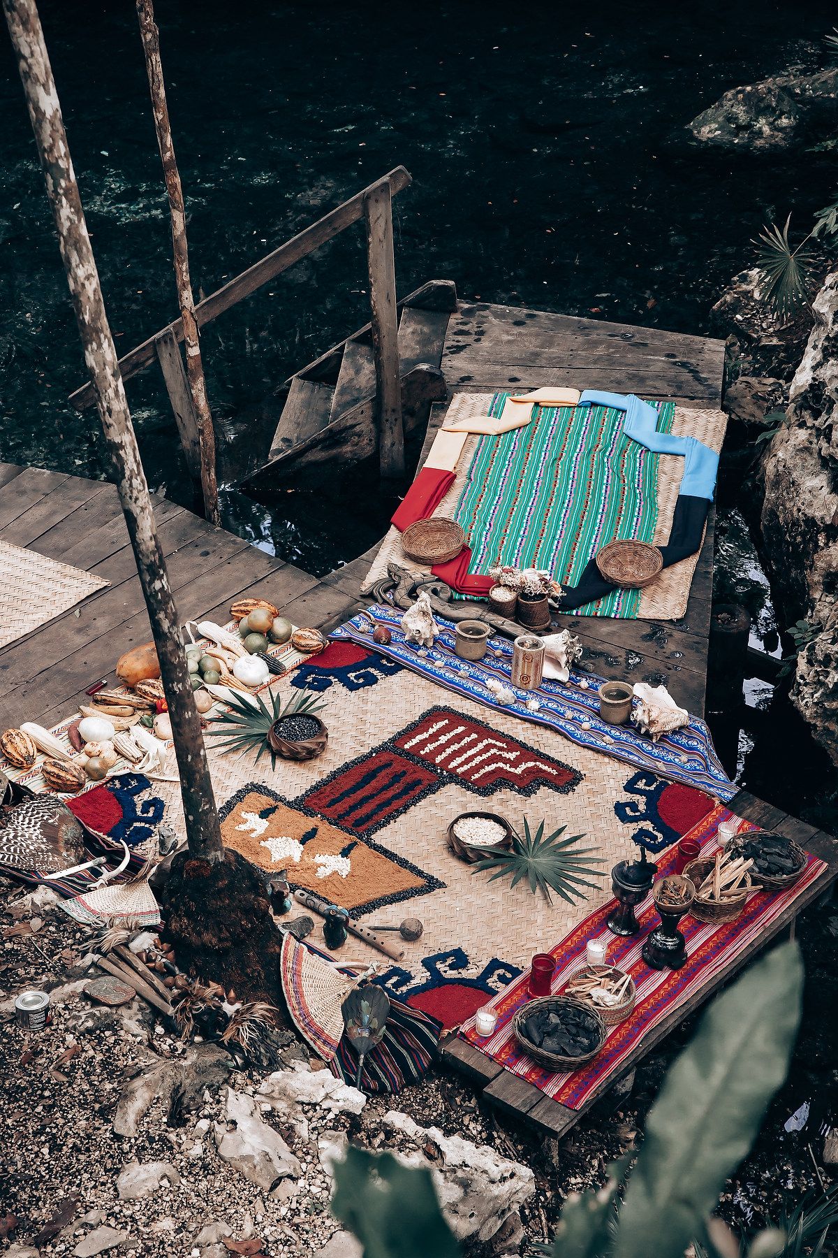Bohemian picnic setup with colorful rugs and blankets laid out on forest ground.