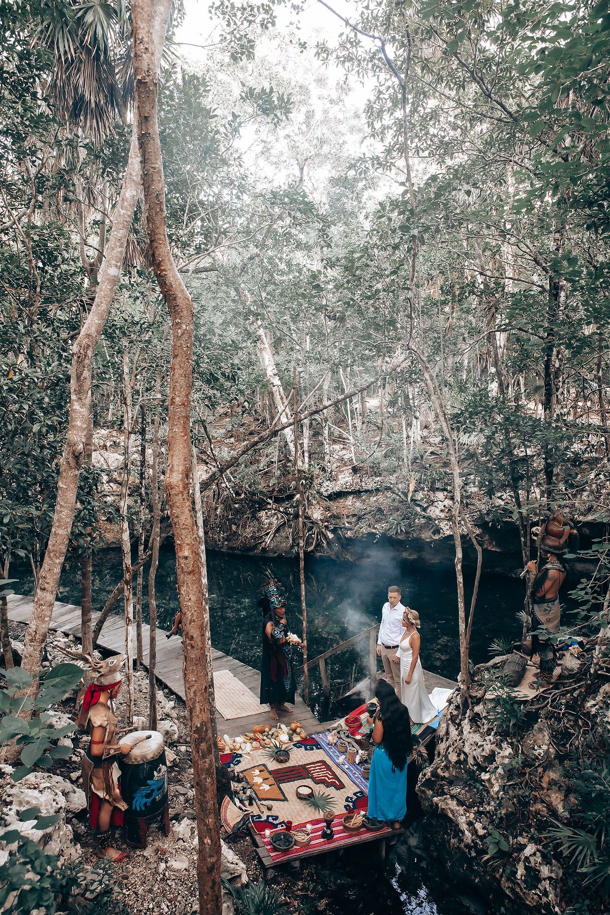 People gather for a picnic in a wooded forest area with blankets spread on rocky ground.