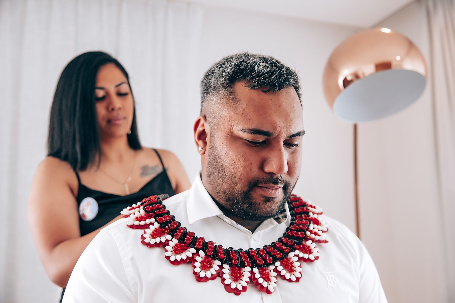 A group wearing white outfits and red beaded necklaces poses together in a celebratory moment.