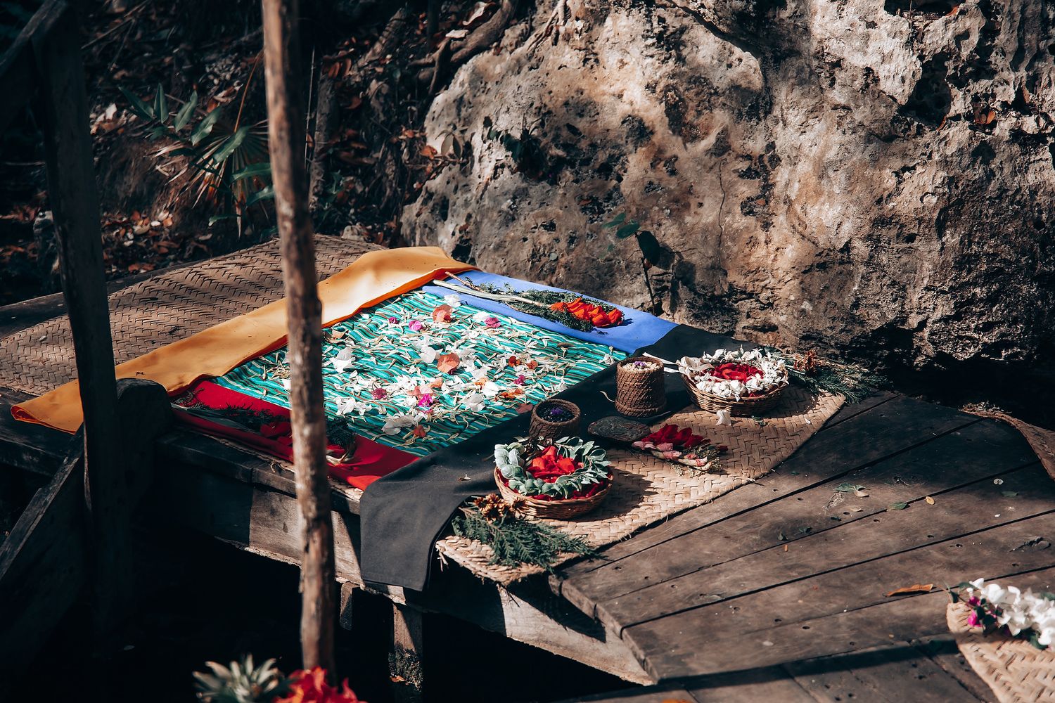Colorful blankets and cushions create a cozy picnic setup against a rocky cave wall backdrop.
