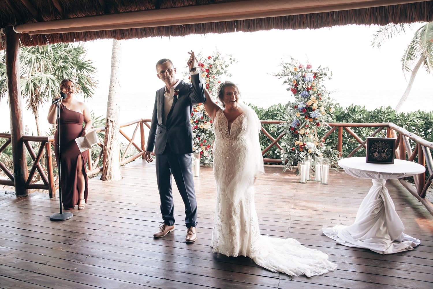 Newlyweds celebrate their first dance under a thatched pavilion with colorful floral arrangements.