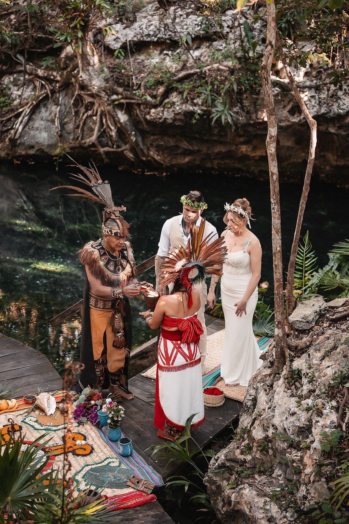 Couple exchanges vows in a Mayan ceremony by a cenote, officiated by traditional shamans in headdresses.