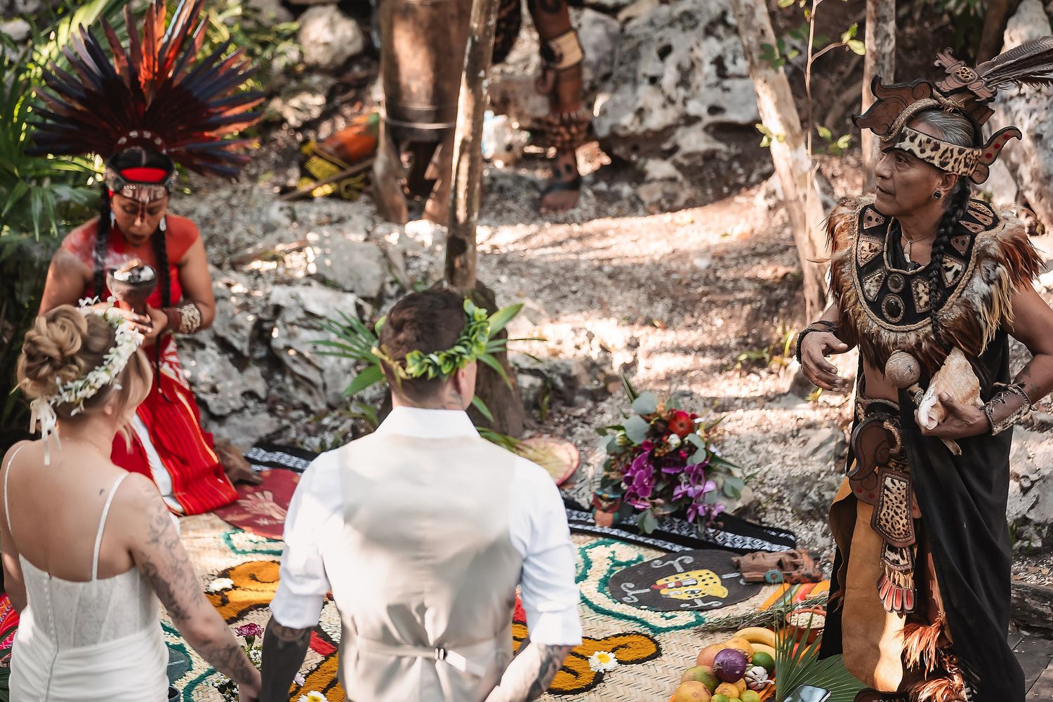 Mayan wedding ceremony in jungle with officiant in traditional costume and couple in white attire.