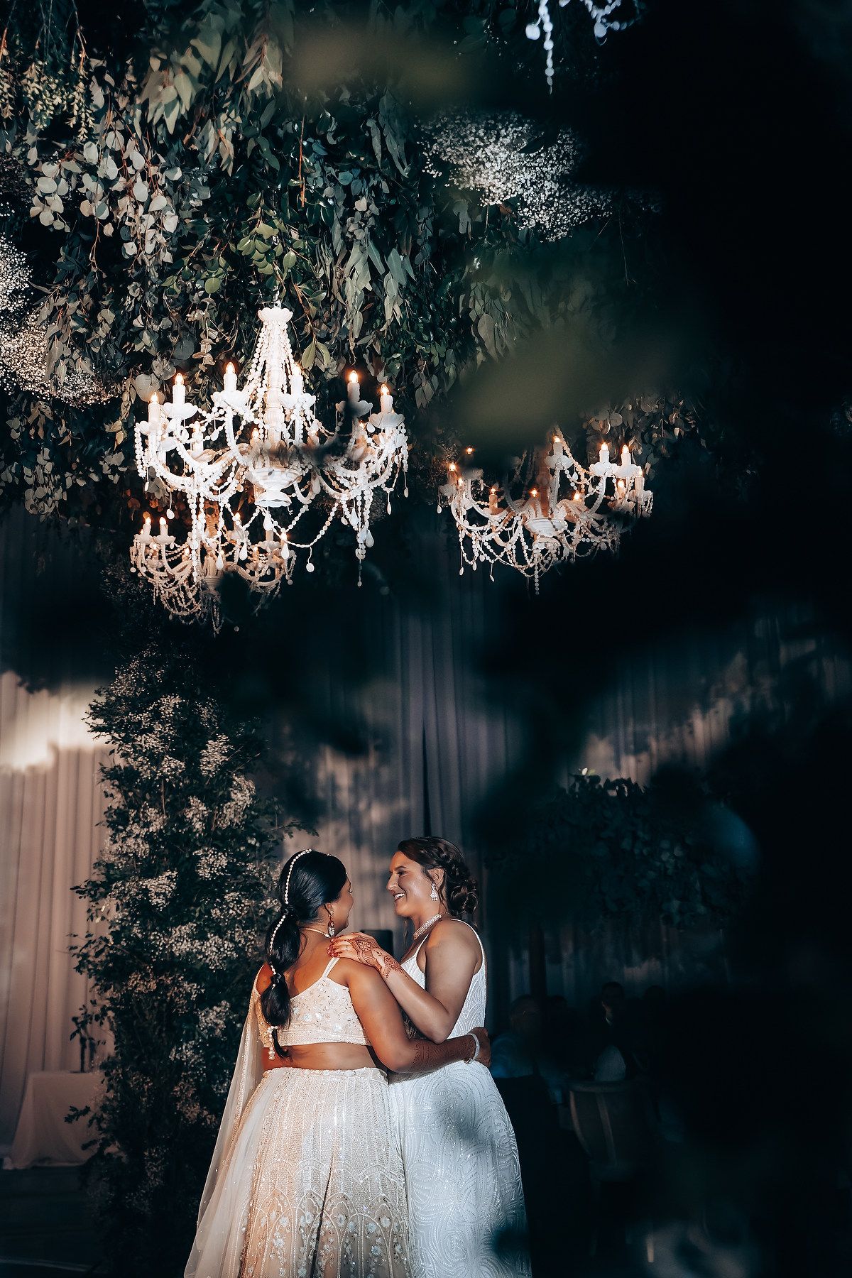 Crystal chandeliers and greenery create a magical canopy above an elegant wedding reception space.