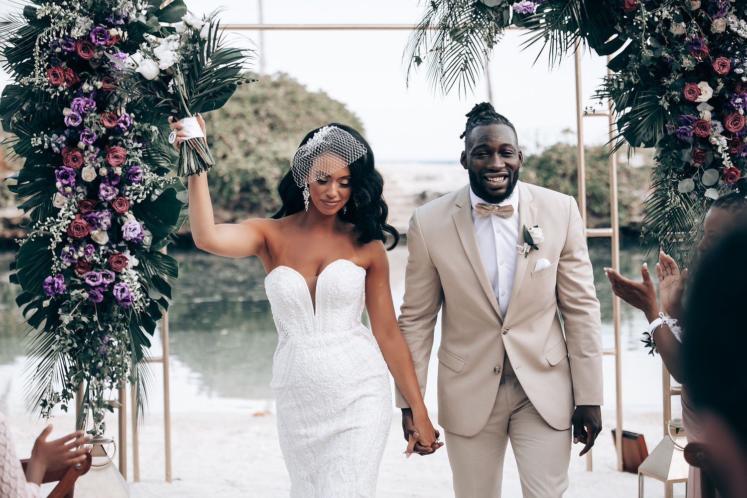 Joyful wedding celebration with bridal party walking under floral arch decorations.