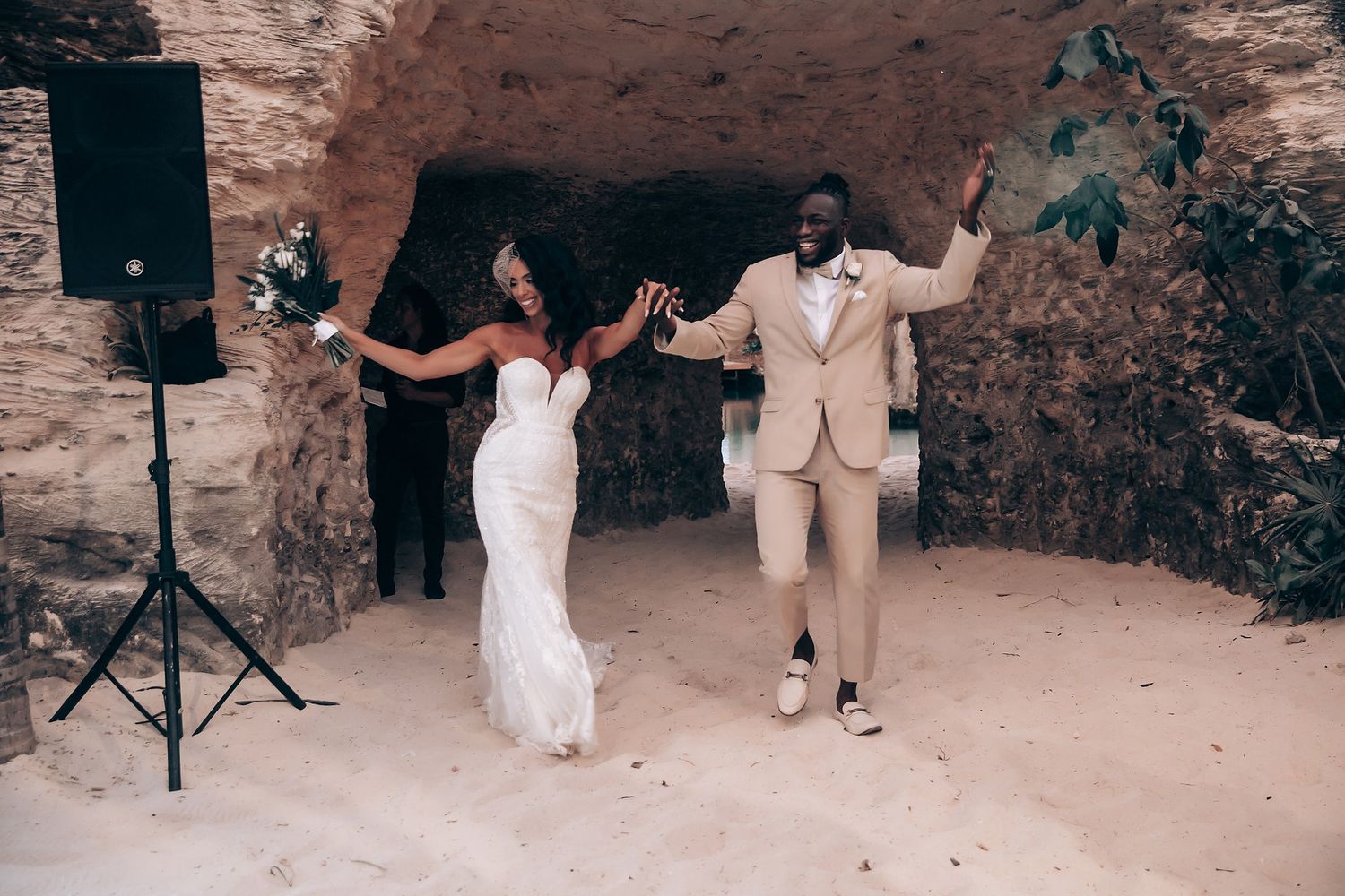 Newlyweds dance joyfully in cave-like setting with speaker system.