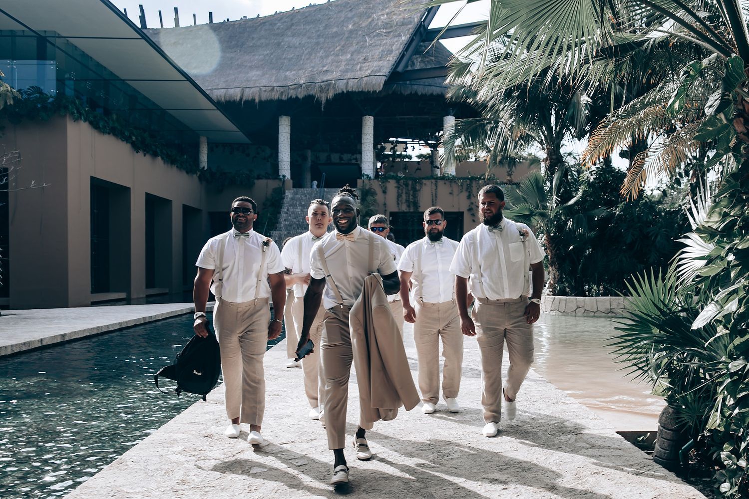 Wedding party members walking together in khaki and white attire beside a reflecting pool.