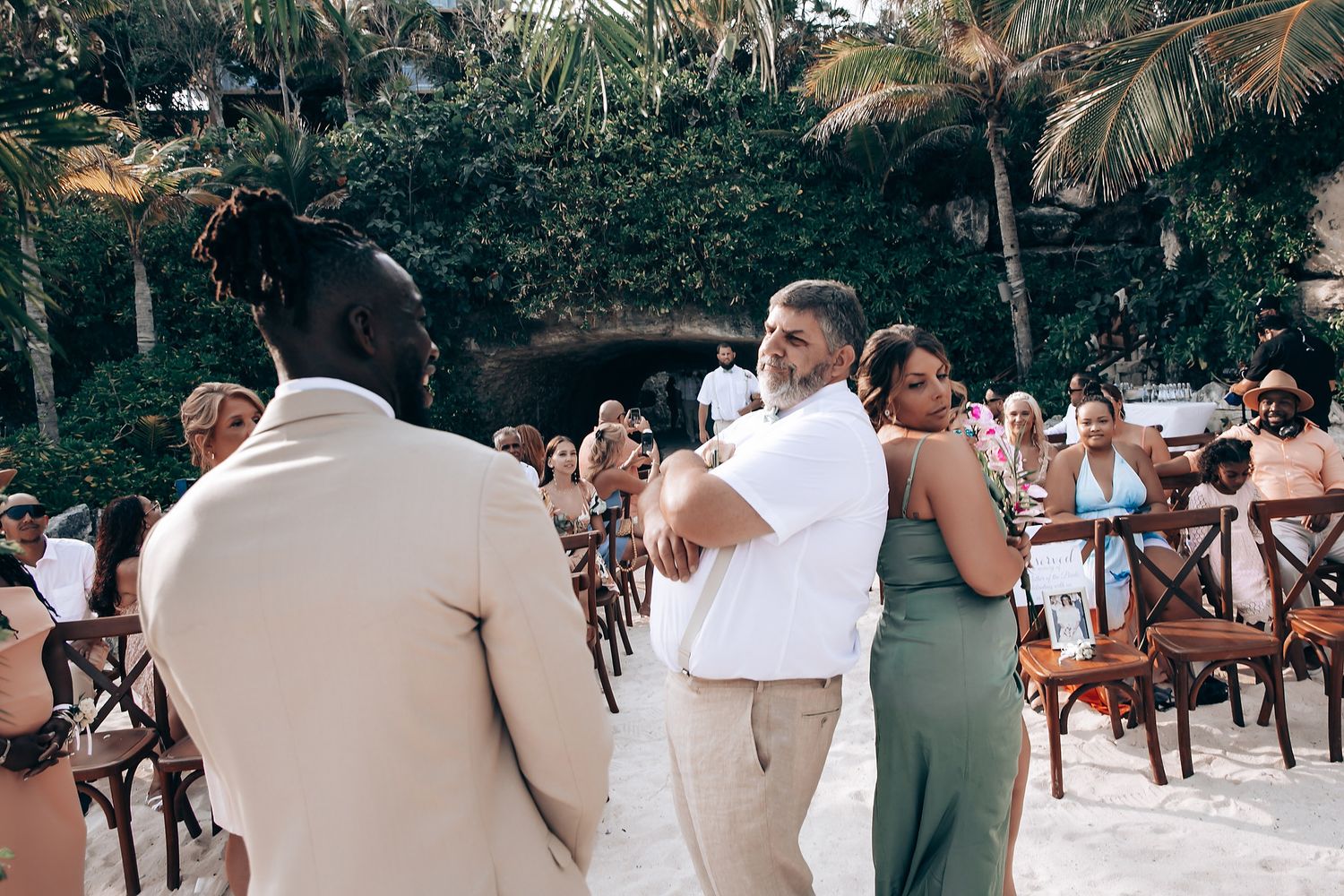 Wedding guests seated in wooden chairs at an outdoor tropical ceremony.