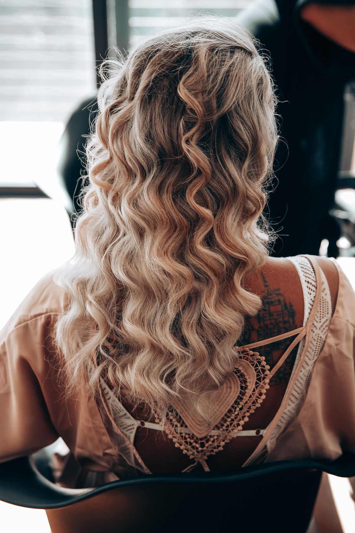 Close-up view of blonde wavy hair and intricate lace detail on the back of a formal dress.