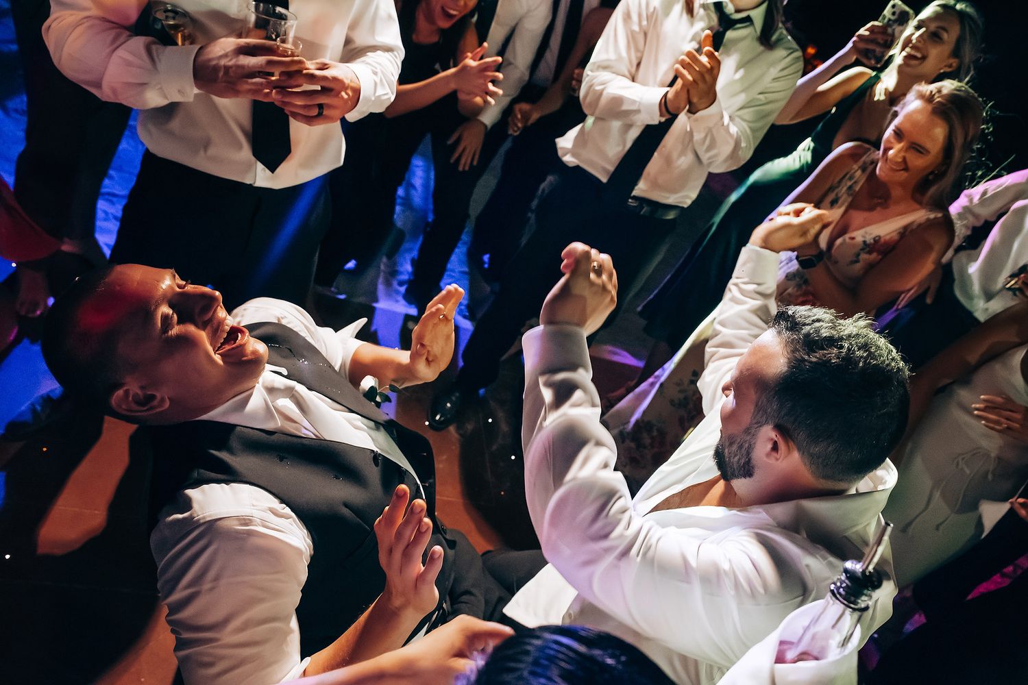 Wedding reception dance floor filled with guests dancing and celebrating under blue lighting.